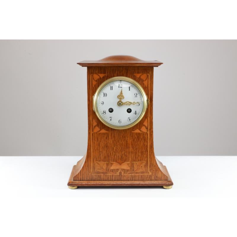Liberty and Co. London. An Arts and Crafts oak mantle clock with floral inlay. The dome top and architectural style of the design of this clock point to the influence C F A Voysey.
