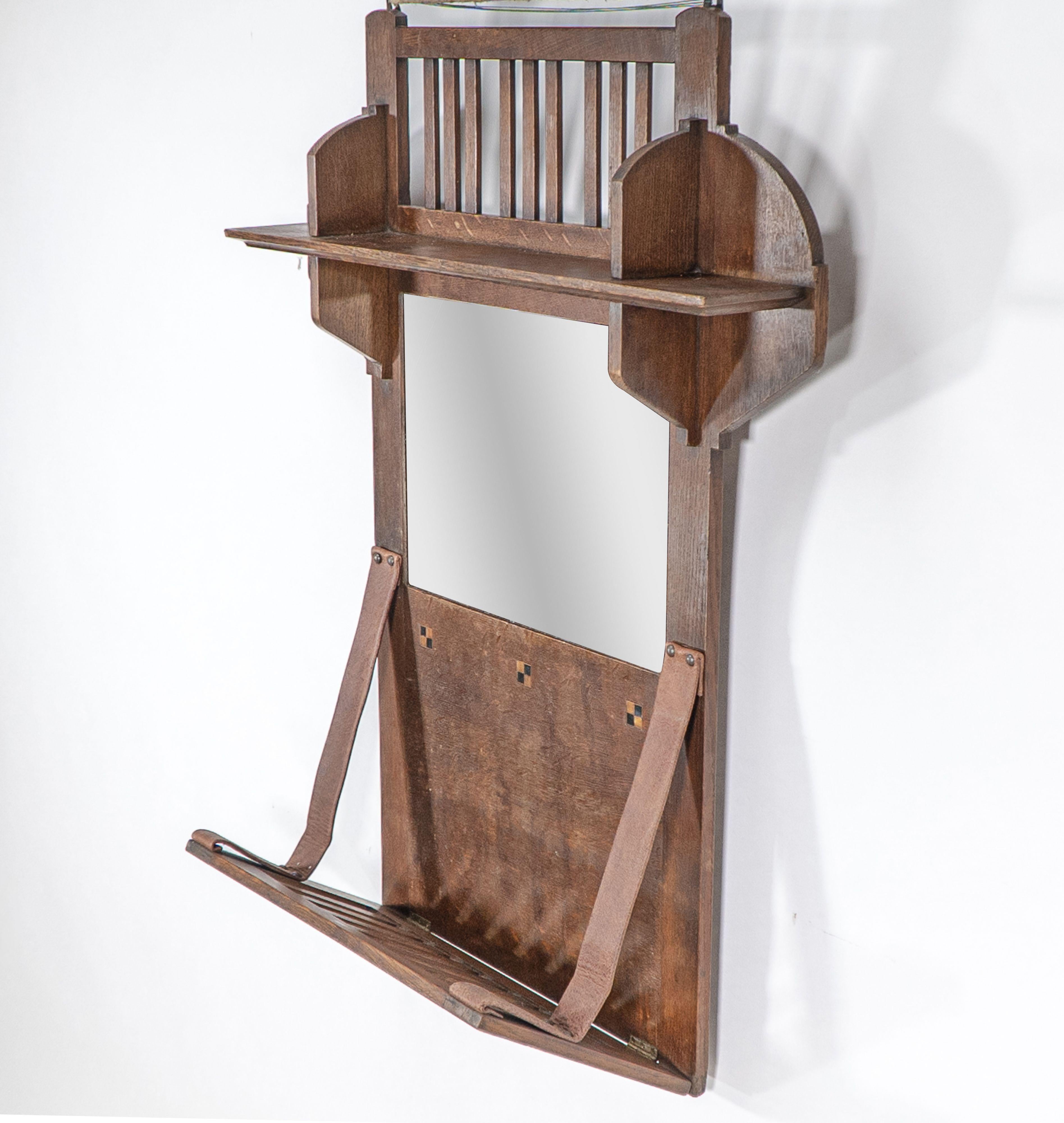 Liberty und Co. Ein Hängeregal aus Eichenholz im Arts & Crafts-Stil mit zentralem Spiegel, oberer Ablage und quadratischen Intarsien aus Ebenholz und Buchsbaum, das Ablagefach mit Lederriemen.