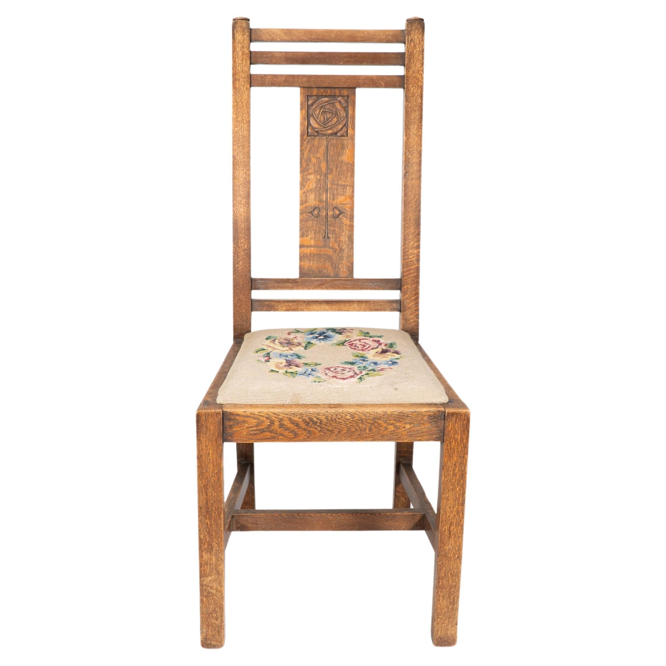 Liberty and Co. An Arts and Crafts oak chair with carved rose decoration to the back, the drop-in seat with colorful embroidery. We also have a matching Liberty and Co gate leg dining table available in another listing.