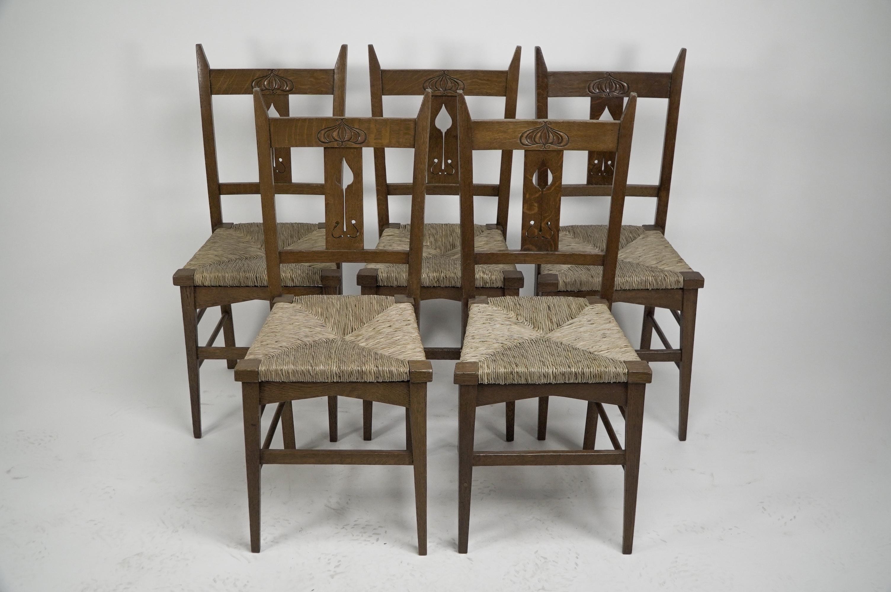 Liberty and Co attributed. A set of six Glasgow Style oak dining chairs consisting of one armchair and five side chairs with floral carving to the head rests and a single flower cut-out to the back rests with square tapering legs to the front united