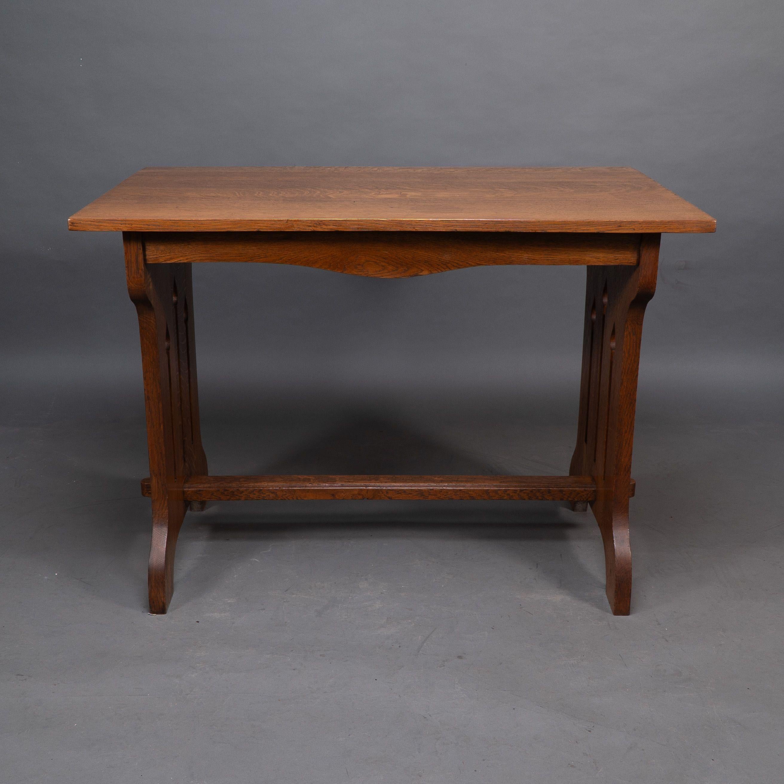Liberty and Co attributed. An Arts and Crafts quarter sawn oak dining or library table showing good figuring to the grain, with three vertical tulip style cut-outs to each end. The stretcher with through pegged joints.