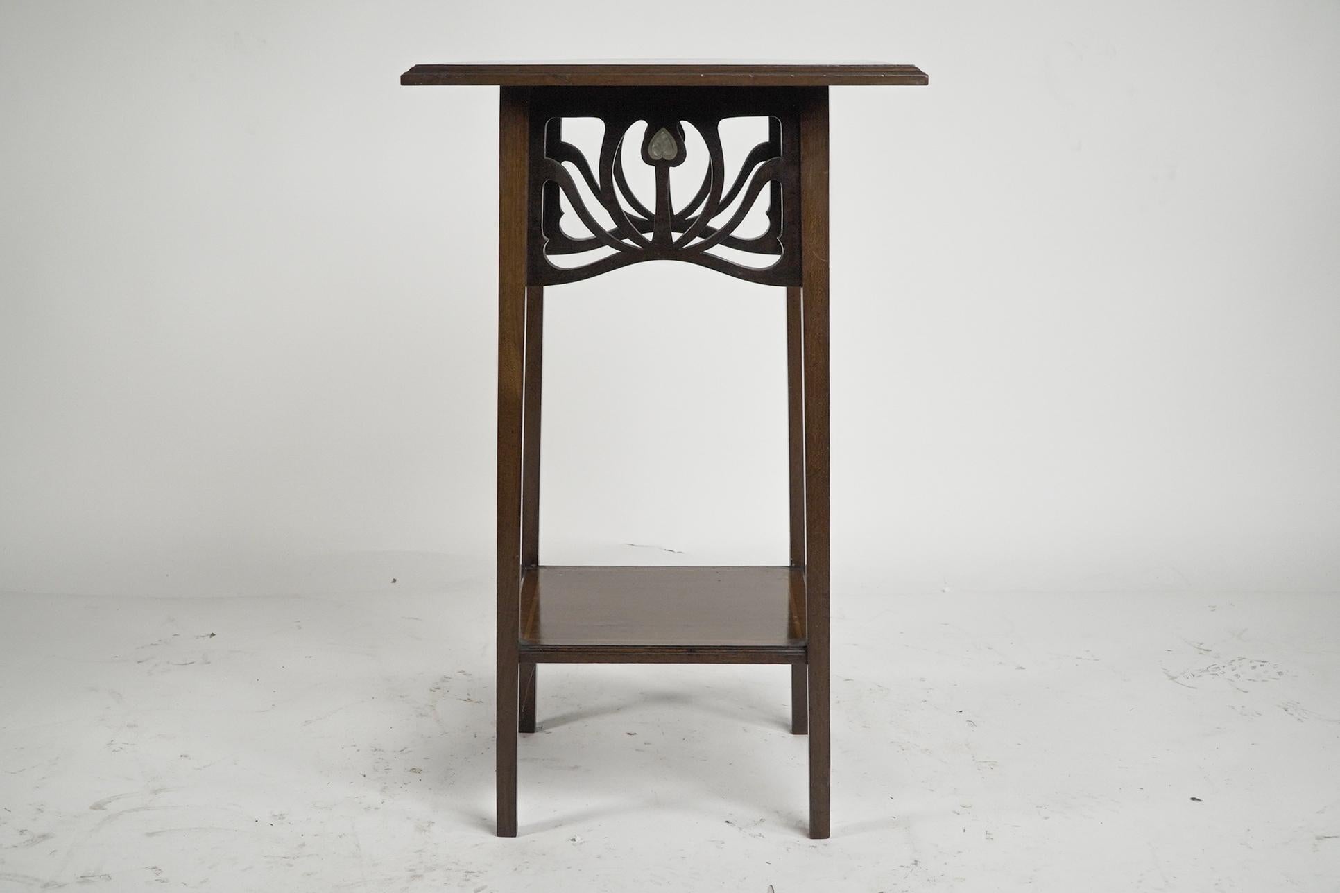 Liberty and Co, attributed. An Arts and Crafts Mahogany occasional table with Mother-Of-Pearl hearts inlaid to the four corners of the molded top united by Sycamore line inlays, with an Art Nouveau flowing fretwork decoration below to each side each