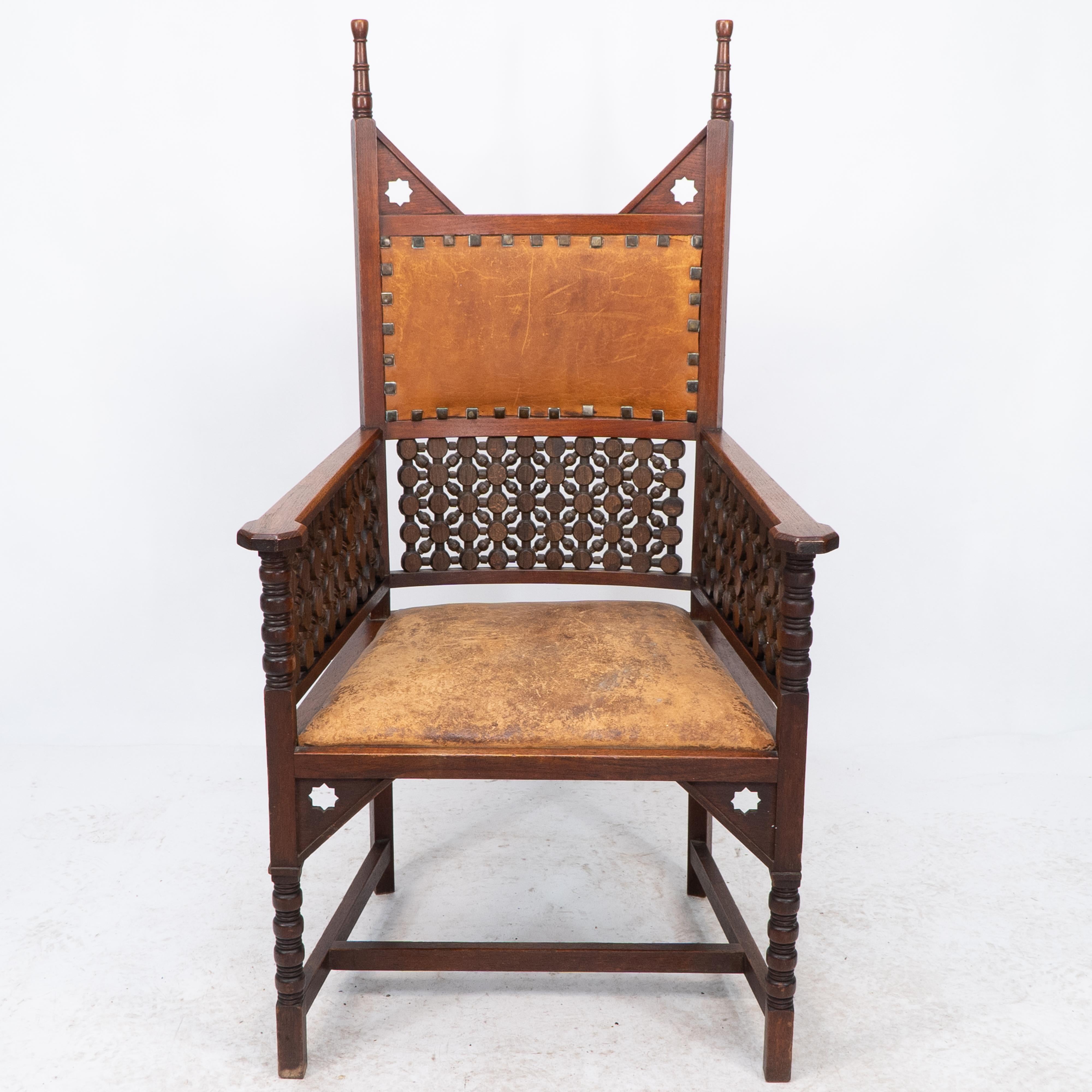 Liberty and Co. A Moorish high-back walnut armchair with elongated turned finials and triangular upper supports to each side pierced with Moorish devices. Under the shaped arms and under the leather backrest are Musharabieh turnings. Further