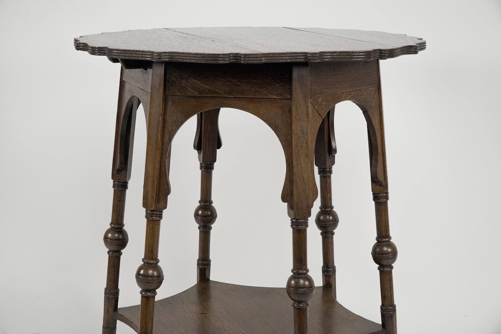 Liberty and Co. An Arts and Crafts oak side or occasional table with a shaped top and molded edges. Six legs with bulbous details uniting with a lower spider web shaped shelf. With original enamel Liberty label underneath the top.