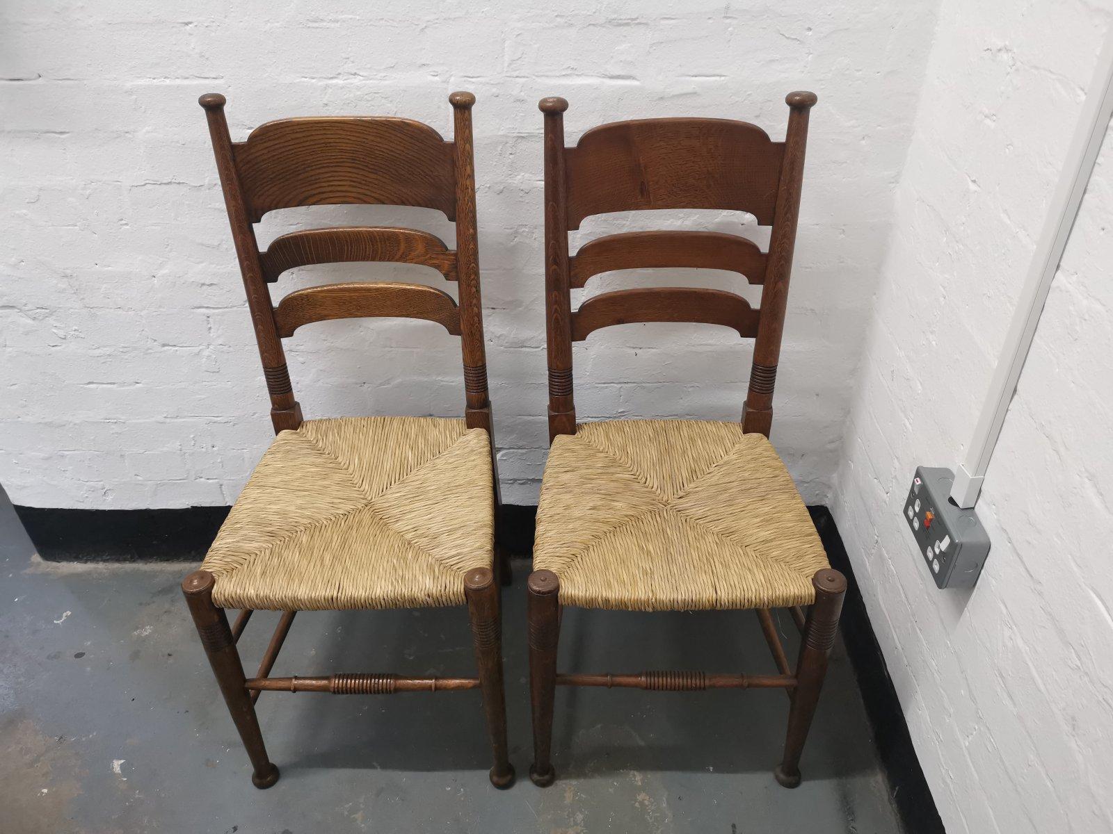 Liberty & Co. Made by William Birch
A pair of English Arts & Crafts oak rush-seat dining chairs. 
These chairs have been totally restored and had new rush professionally laid to the seat. To professionally re-rush a chair seat demands a good deal of