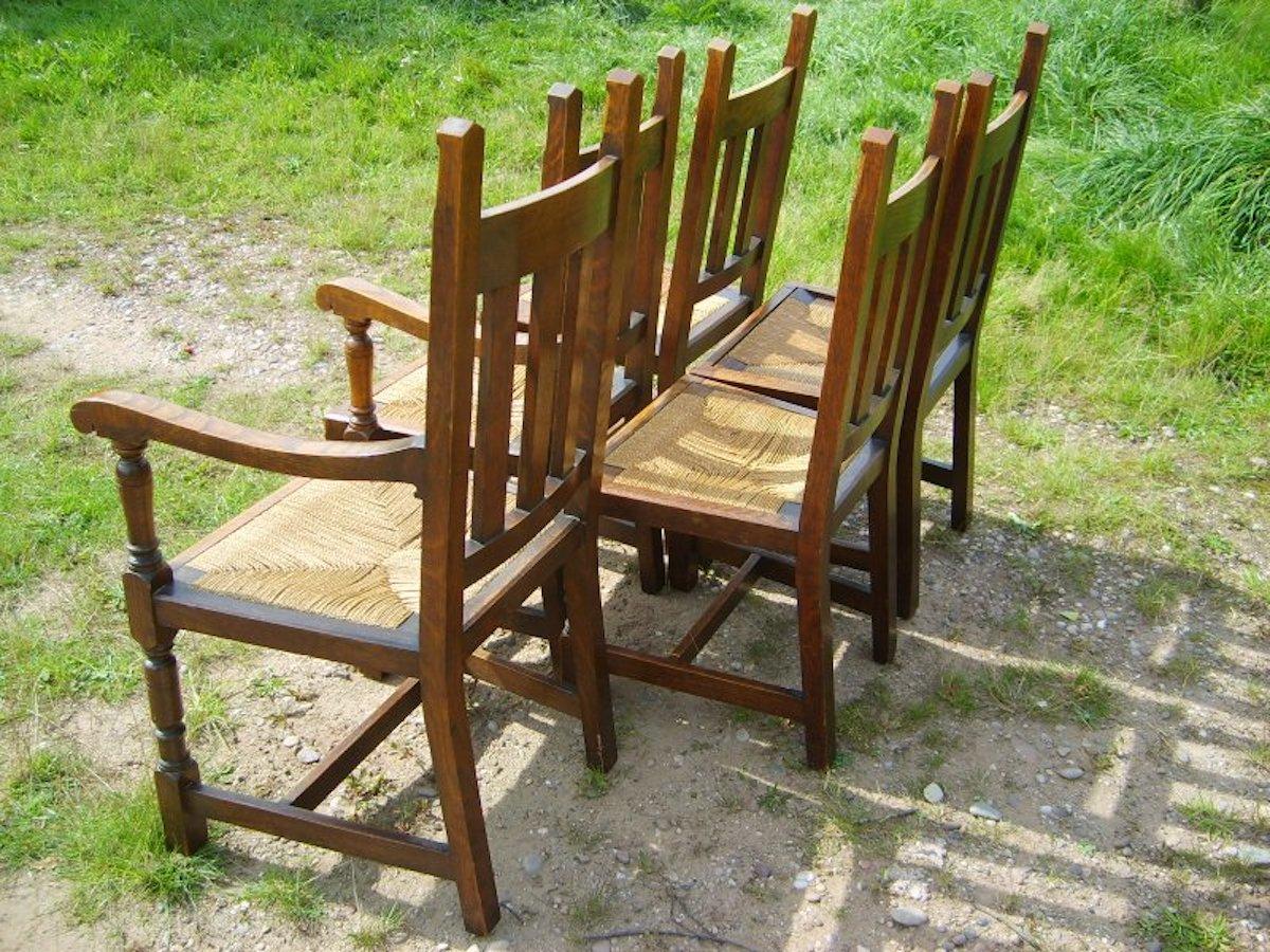 Liberty and Co. Ensemble de six chaises de salle à manger en chêne de style Arts & Crafts à assise en jonc, avec des détails en forme de flèche sur les plateaux et des pieds tournés réunis par une traverse en H.
Deux fauteuils et quatre lits