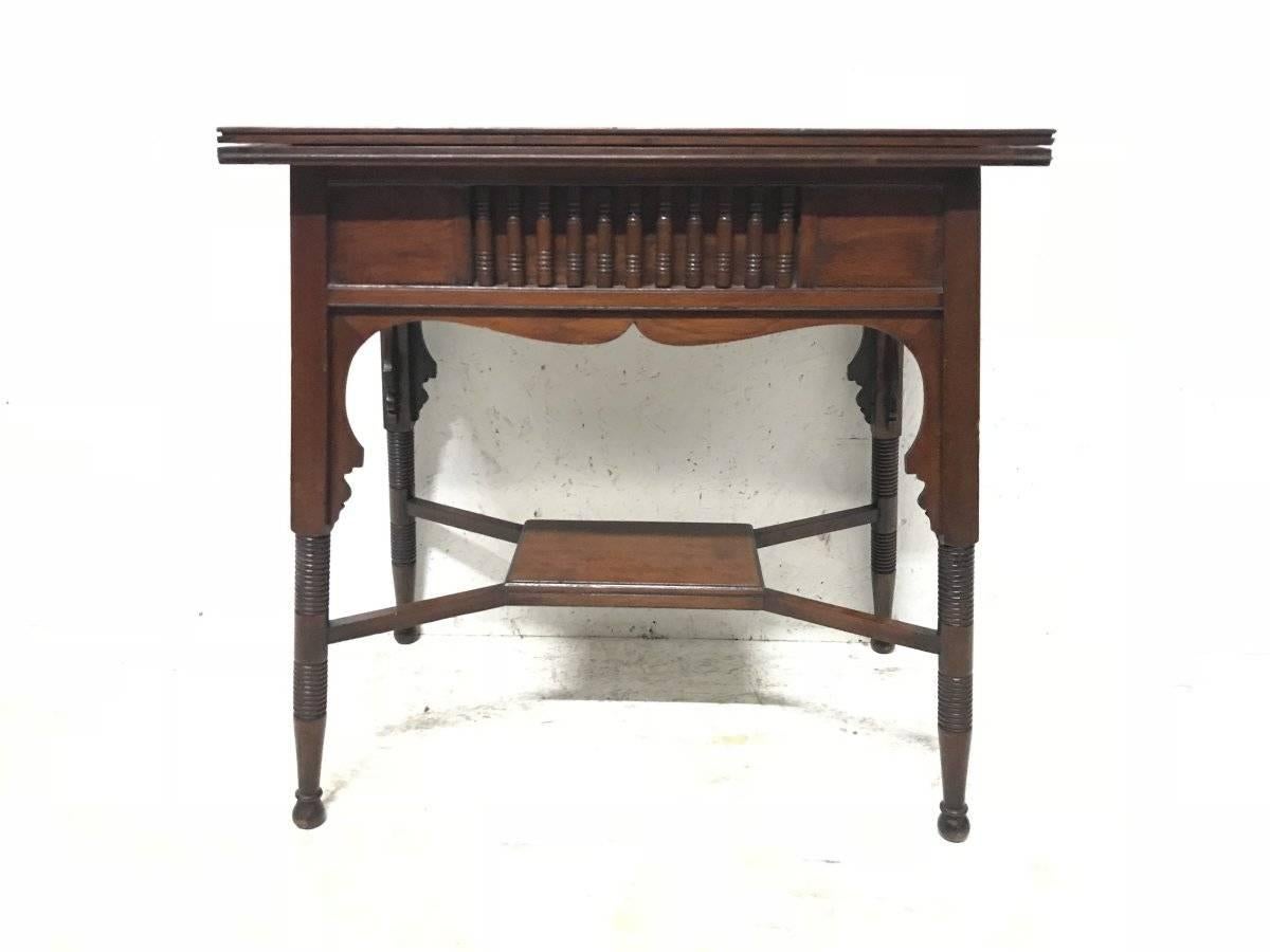 Liberty & Co. an Anglo-Moorish Arts & Crafts fold over card and games table in Walnut with green baize interior when open. Turned details to the upper and arched apron with turned and incised legs united by a cross stretcher. There is also an
