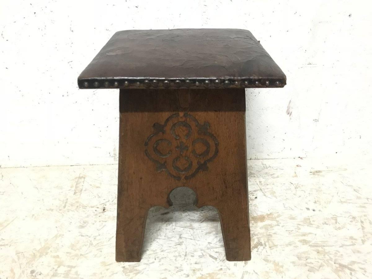 Liberty & Co., an Arts & Crafts oak stool with original embossed leather seat depicting flowers in bloom with stylized carved devices to all four sides and Moorish arched details.