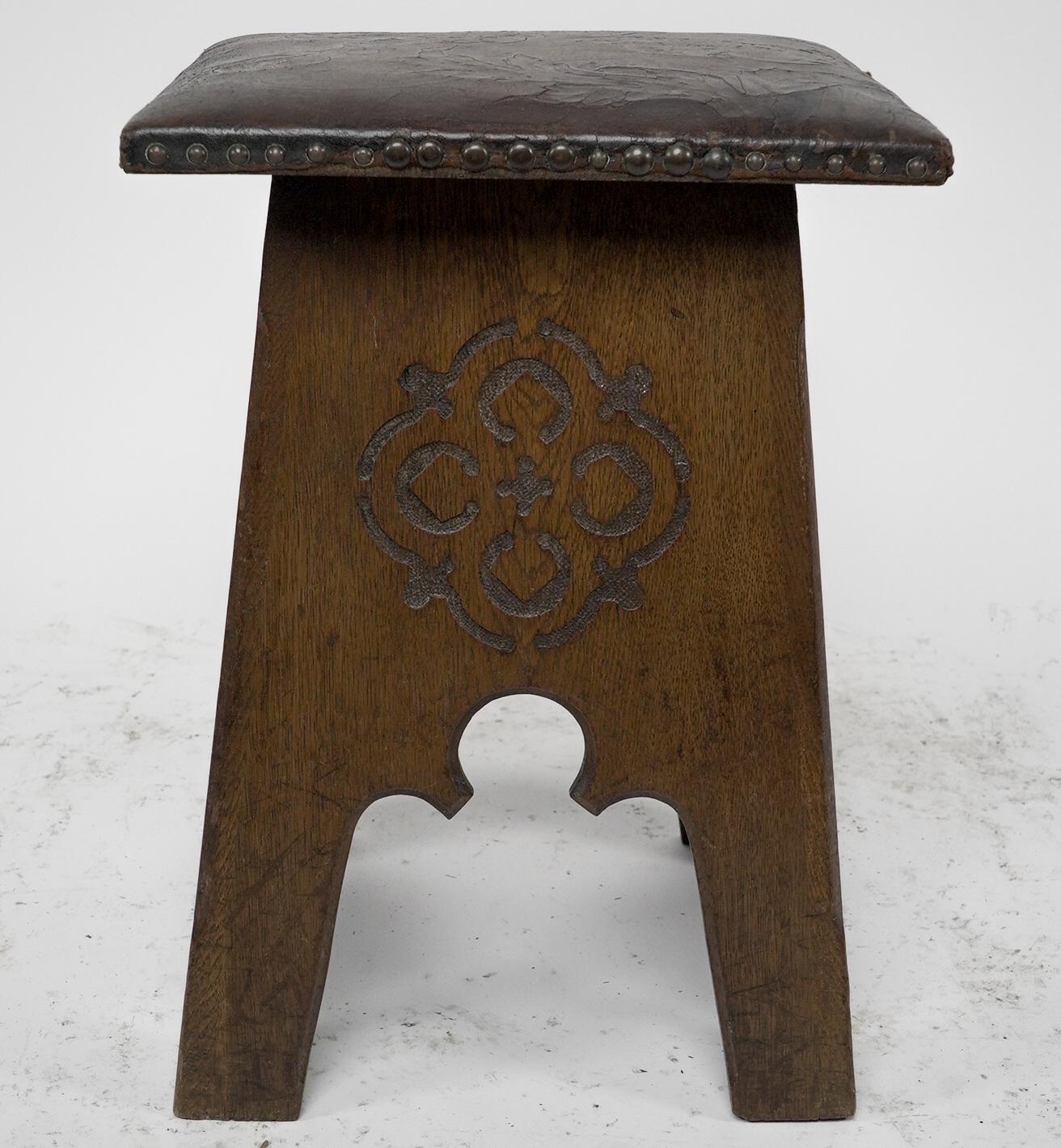 Liberty & Co., an Arts & Crafts oak stool with original embossed leather seat depicting flowers in bloom with stylized carved devices to all four sides and Moorish arched details.