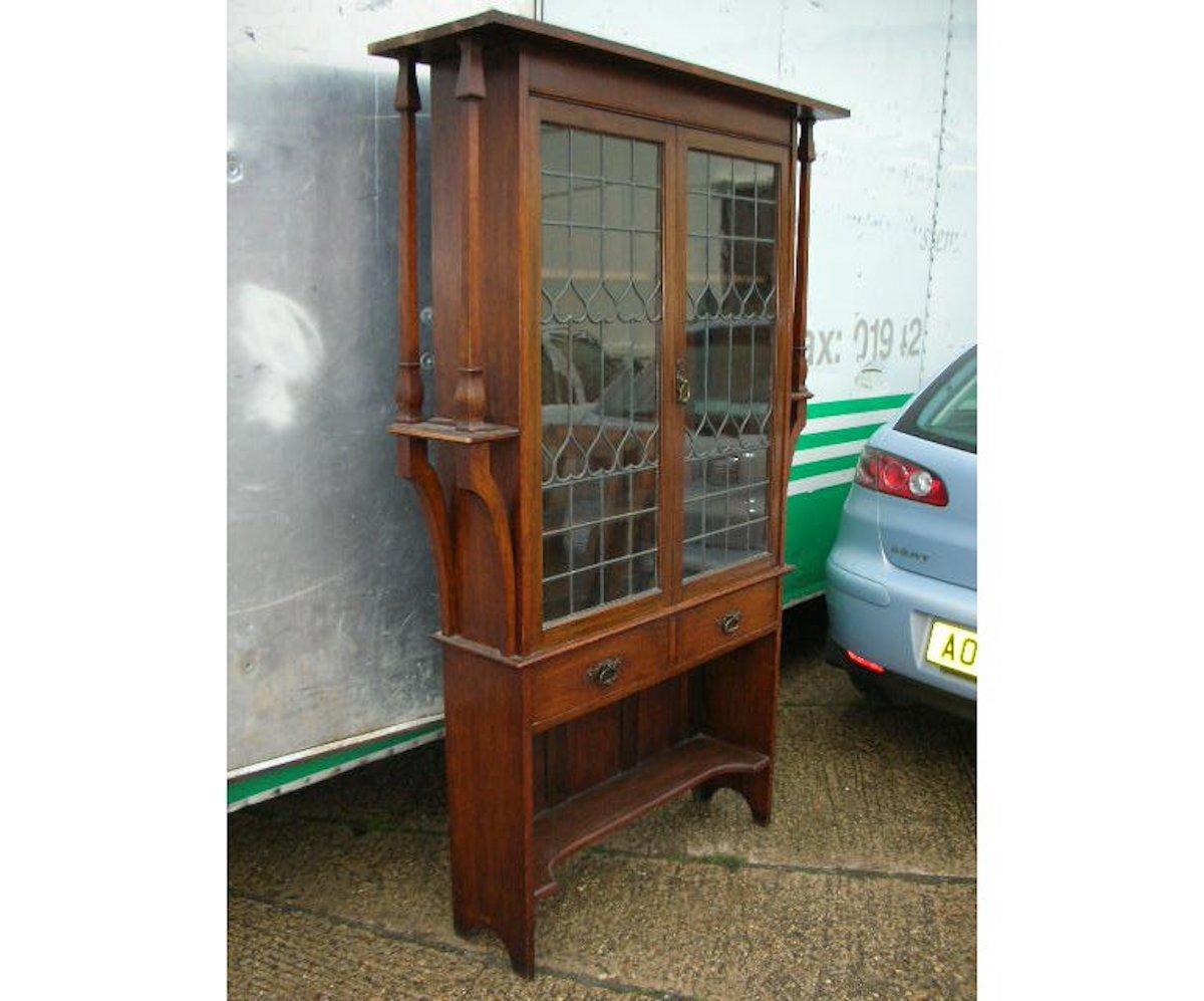 Liberty & Co. A quality Arts & Crafts oak glazed bookcase with stylized heart details and stylized copper handles, flanked by side shelves with twin architectural supports united to the cornice. Two drawers to the centre with stylized copper handles