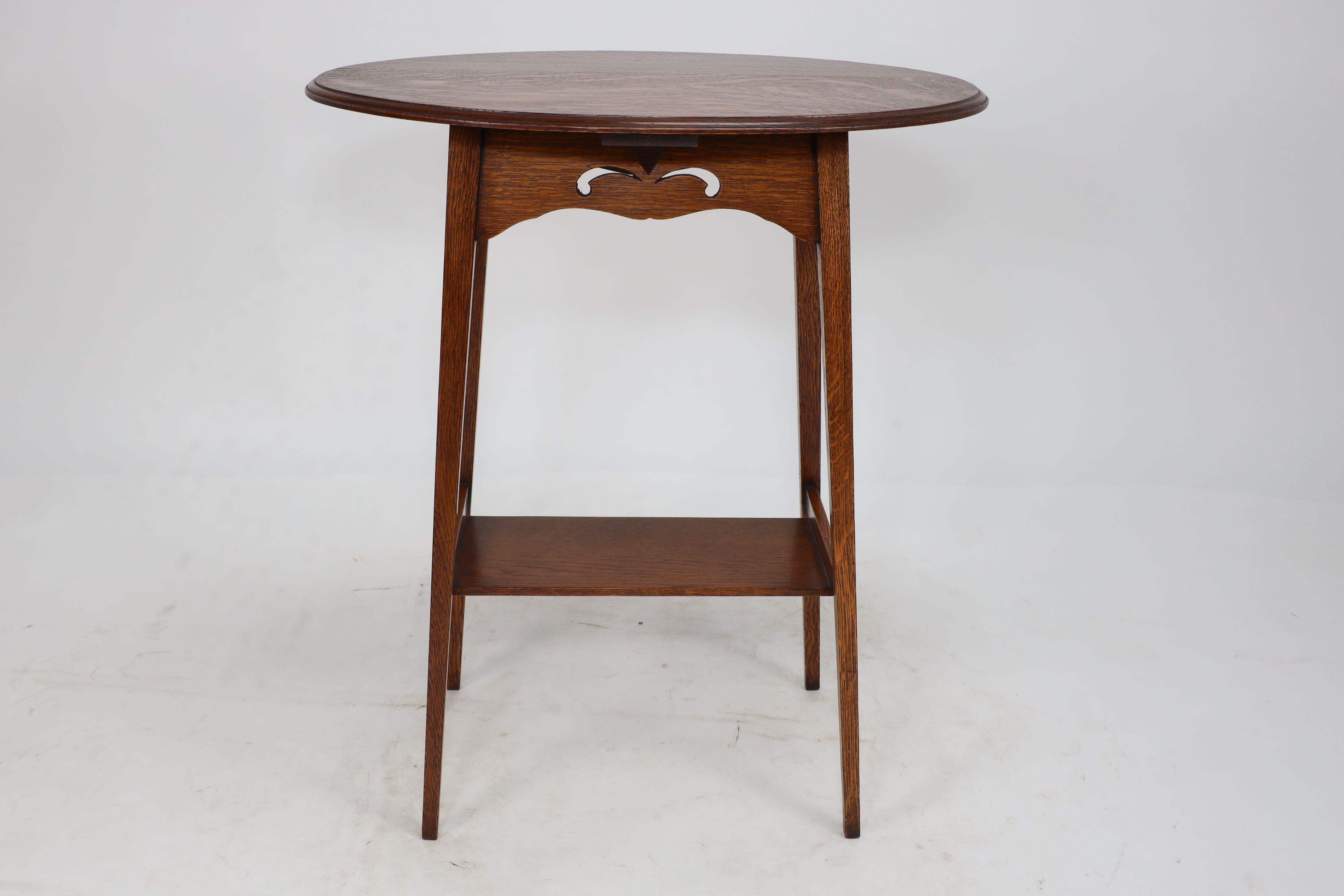 Liberty and Co. An Arts & Crafts oak oval top side table, with stylised heart cut-outs to the apron and square tapering legs, united by lower shelf.