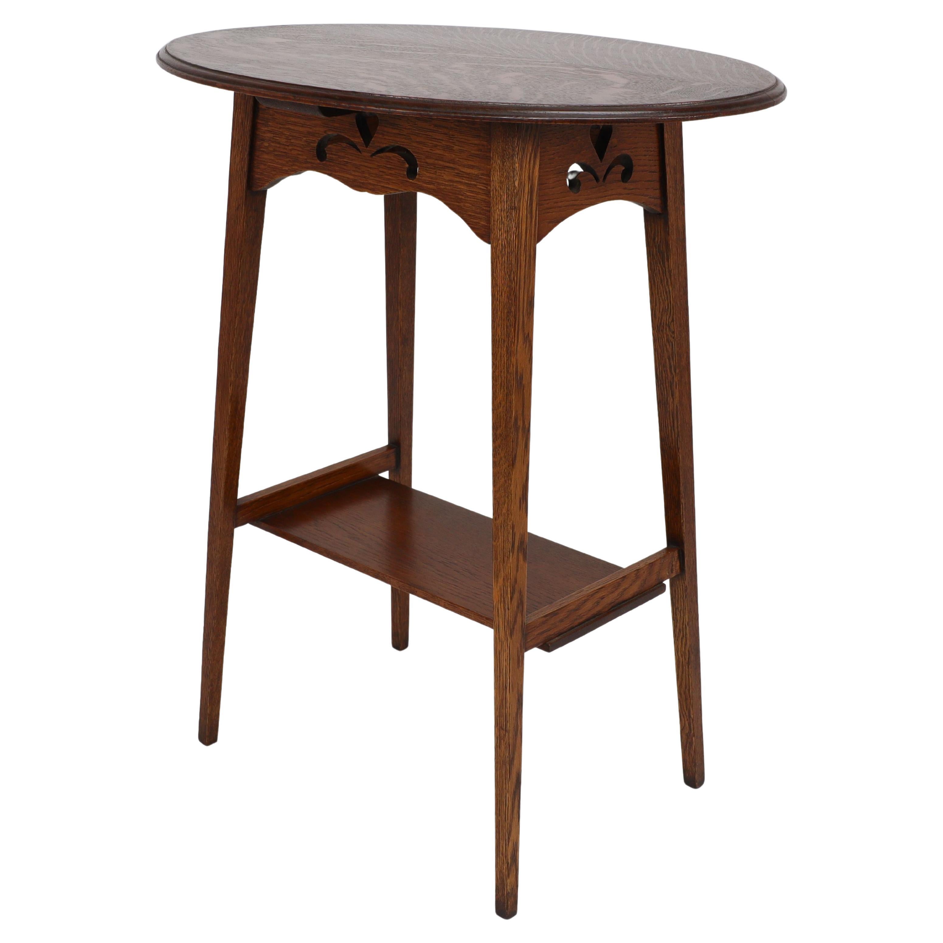 Liberty & Co. An Arts & Crafts oak oval top side table with heart cut-outs