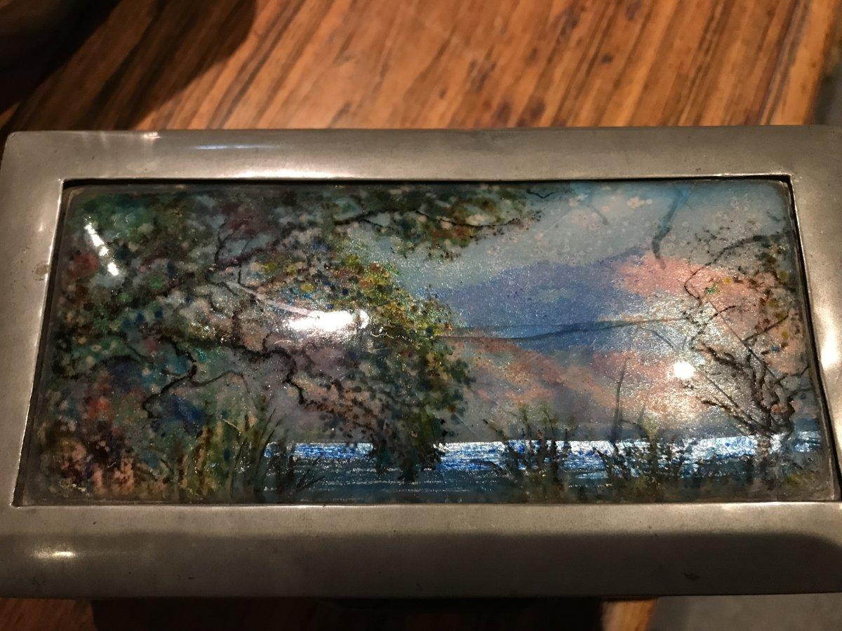 Liberty & Co. an Arts & Crafts pewter and hand enameled jewelry or cigar box.
The enamel work is attributed to Fleetwood Varley.
A country lake scene viewed through a break in the trees and rushes, with glistening silvery blue water and violet and