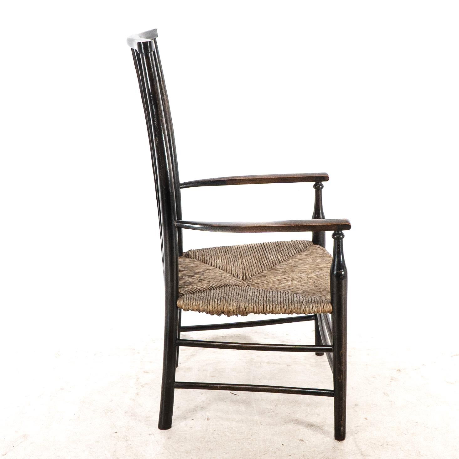 English Liberty & Co. An Arts & Crafts rush seat armchair with wavy shaped back slats For Sale