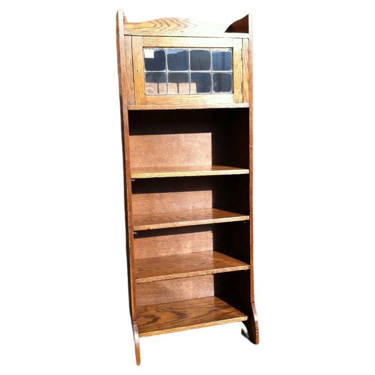 Liberty & Co. An English Arts & Crafts oak bookcase, with shaped upper details.
to the top, leaded glass door to the cupboard, and three open adjustable shelves below, retaining its original Liberty label to the back.
Circa 1900.