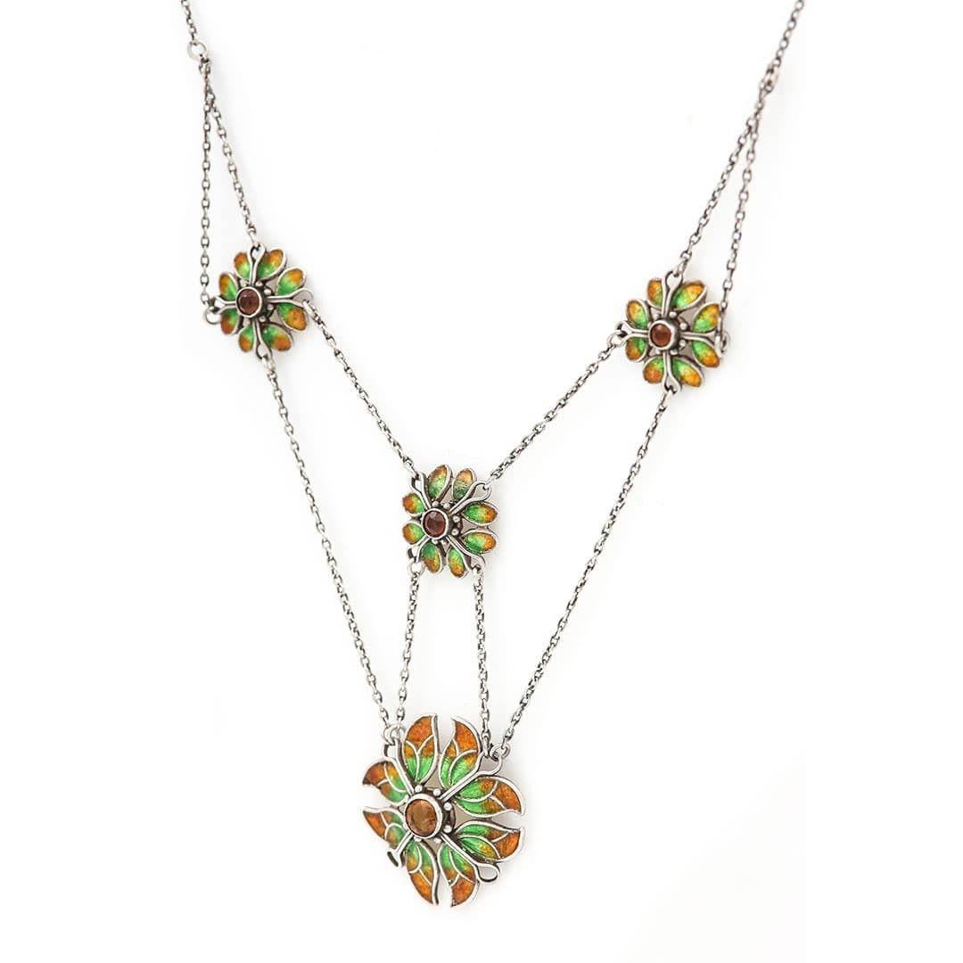 A vibrant Arts and Crafts silver, citrine and enamel necklace designed as four petalled flower heads, made by Liberty and Co. circa 1910. Showing eye-catching iridescent enamelling in emerald green and copper tones this delightful necklet comprises