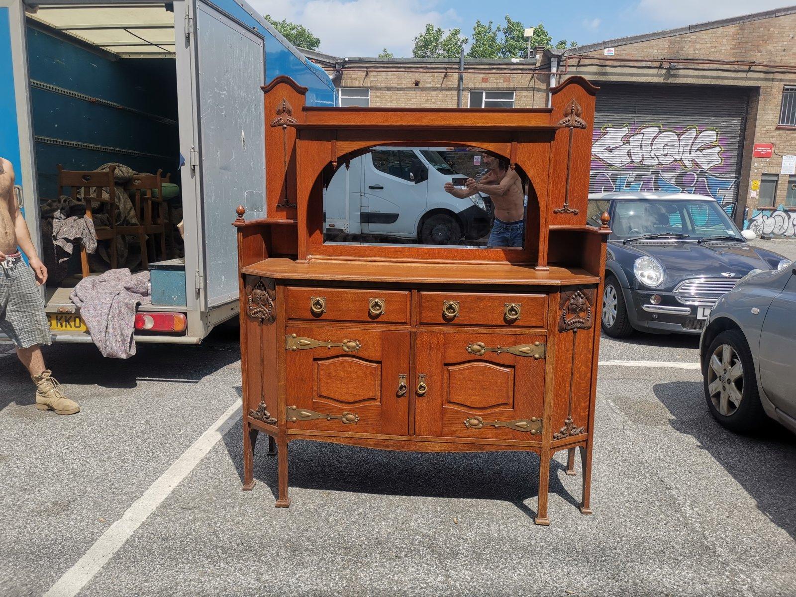 Liberty & Co attributed.
An English Arts & Crafts oak sideboard, with an open upper shelf flanked by stylized carved floral decoration running down each side of the central beveled mirror which is set slightly back behind a fully arched cover with