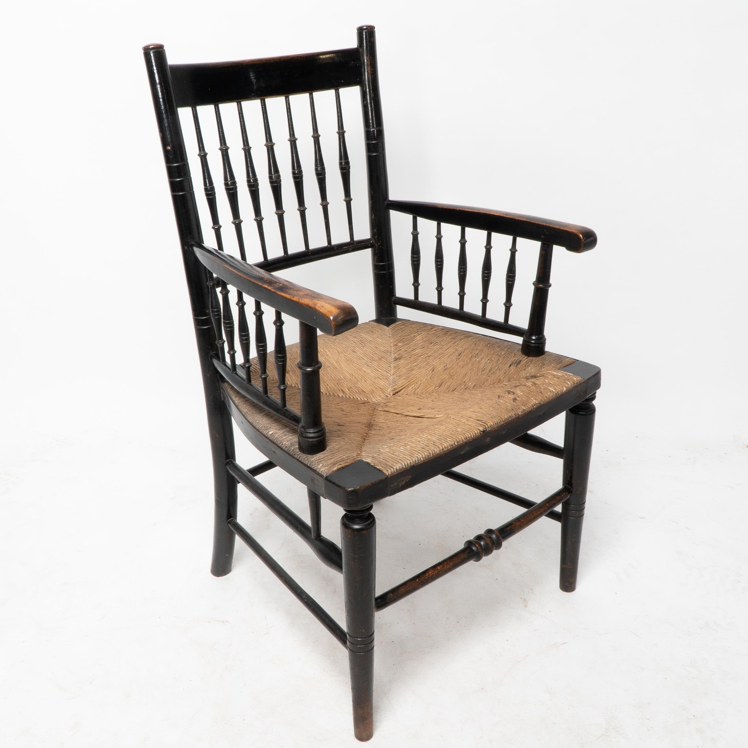 Liberty and Co attribué, style d'un Morris and Co. Fauteuil à assise en jonc du mouvement esthétique, avec des tournures incisées au niveau du dossier et sous les accoudoirs. Les accoudoirs se prolongent jusqu'aux brancards latéraux, comme sur les