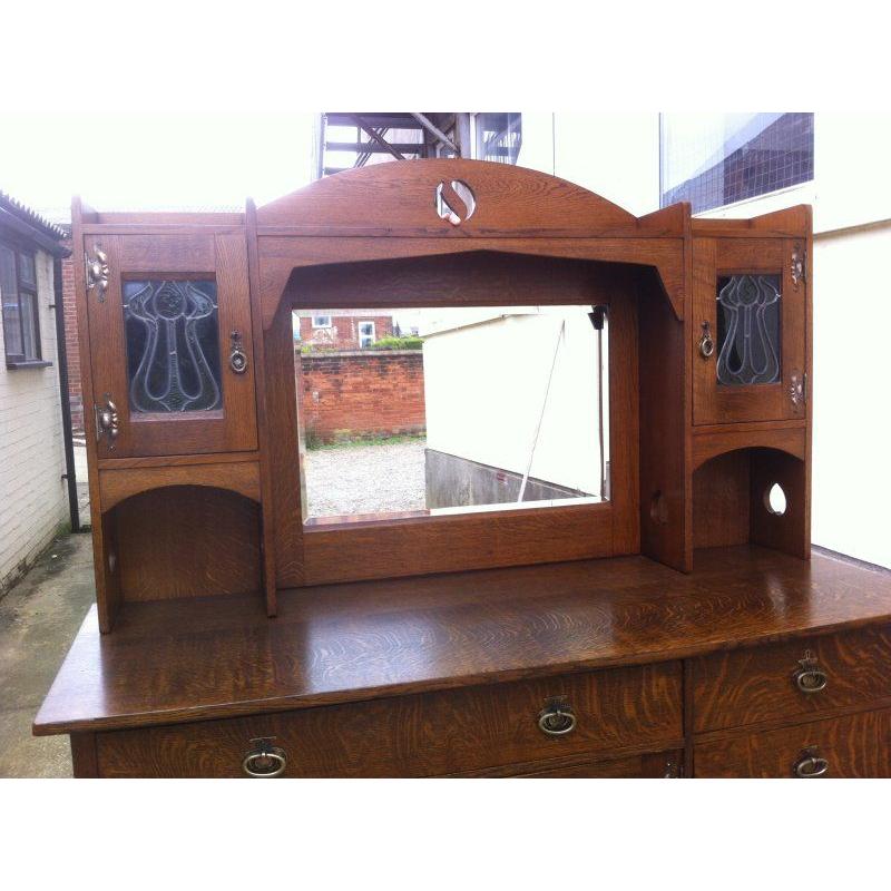Buffet en chêne de style Arts and Crafts, attribué à Liberty and Co, avec une découpe Ying-Yang dans la zone d'exposition supérieure et un miroir biseauté central en dessous, flanqué de portes en verre teinté floral stylisé et de découpes en forme
