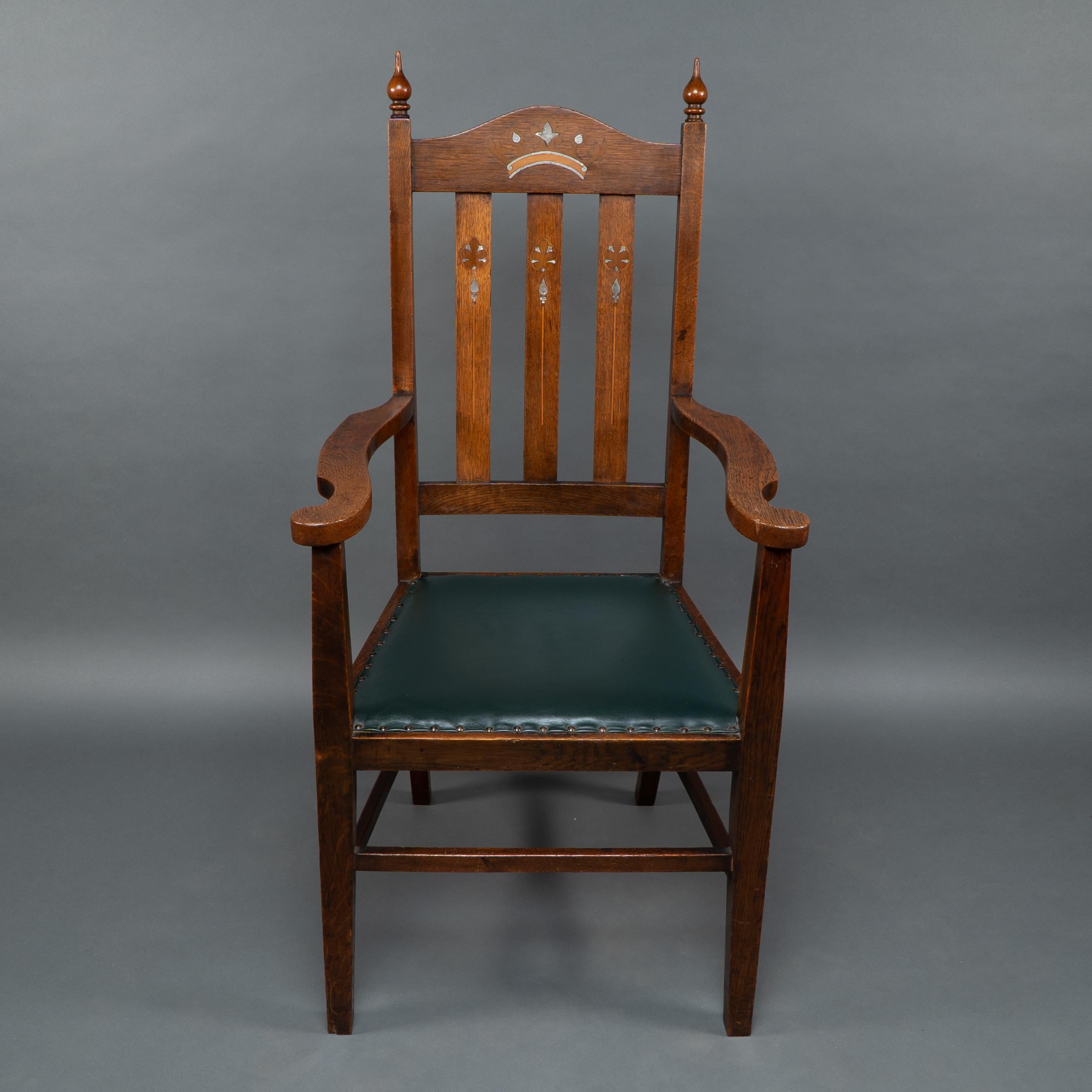 Liberty & Co. atribuida. Sillón Arts and Crafts de roble con corona real en el reposacabezas, incrustaciones de estaño, nogal y maderas frutales y más decoración incrustada en las tablillas del respaldo. Altura del asiento: 47 cm Altura de los