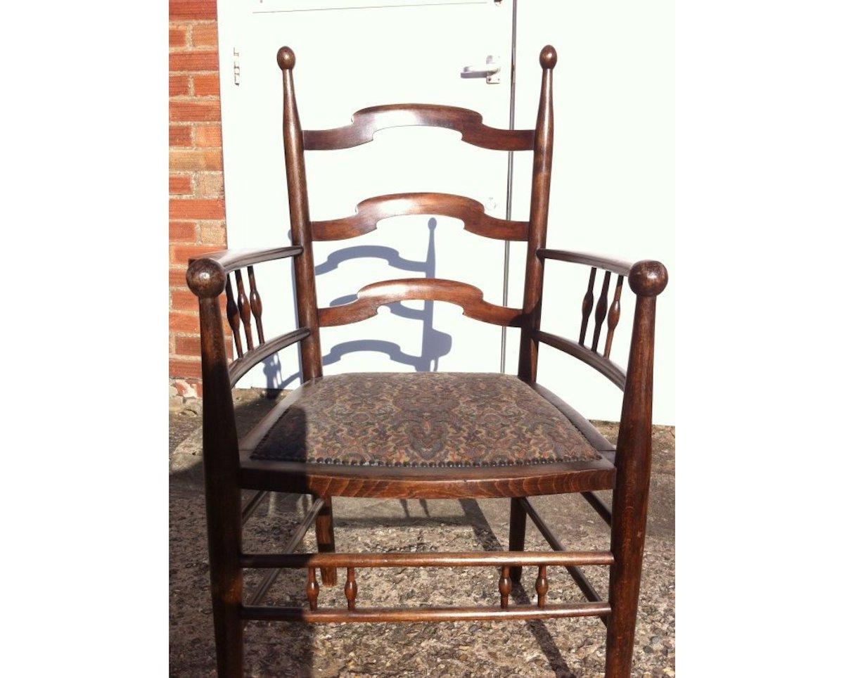 Liberty & Co attributed made by William Birch. 
An English Arts & Crafts shaped ladder back armchair with ball finials to the back and to the front of the arms with turned supports below and further turned supports uniting the stretchers stood on