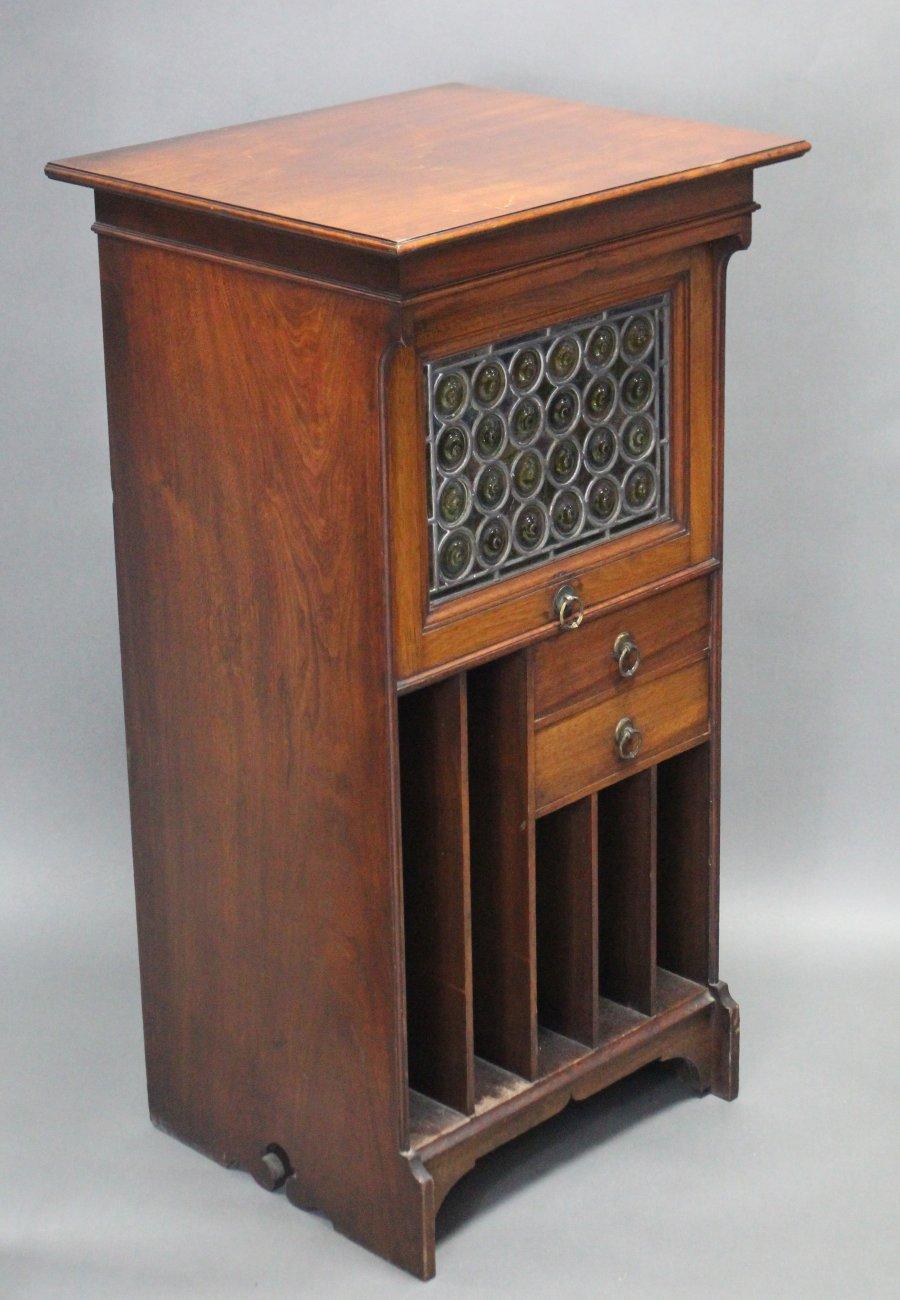 Liberty & Co London. A rare Moorish walnut music cabinet with bottle neck glass up and over door above two side drawers with open slide storage below and typical brass ring pull handles.