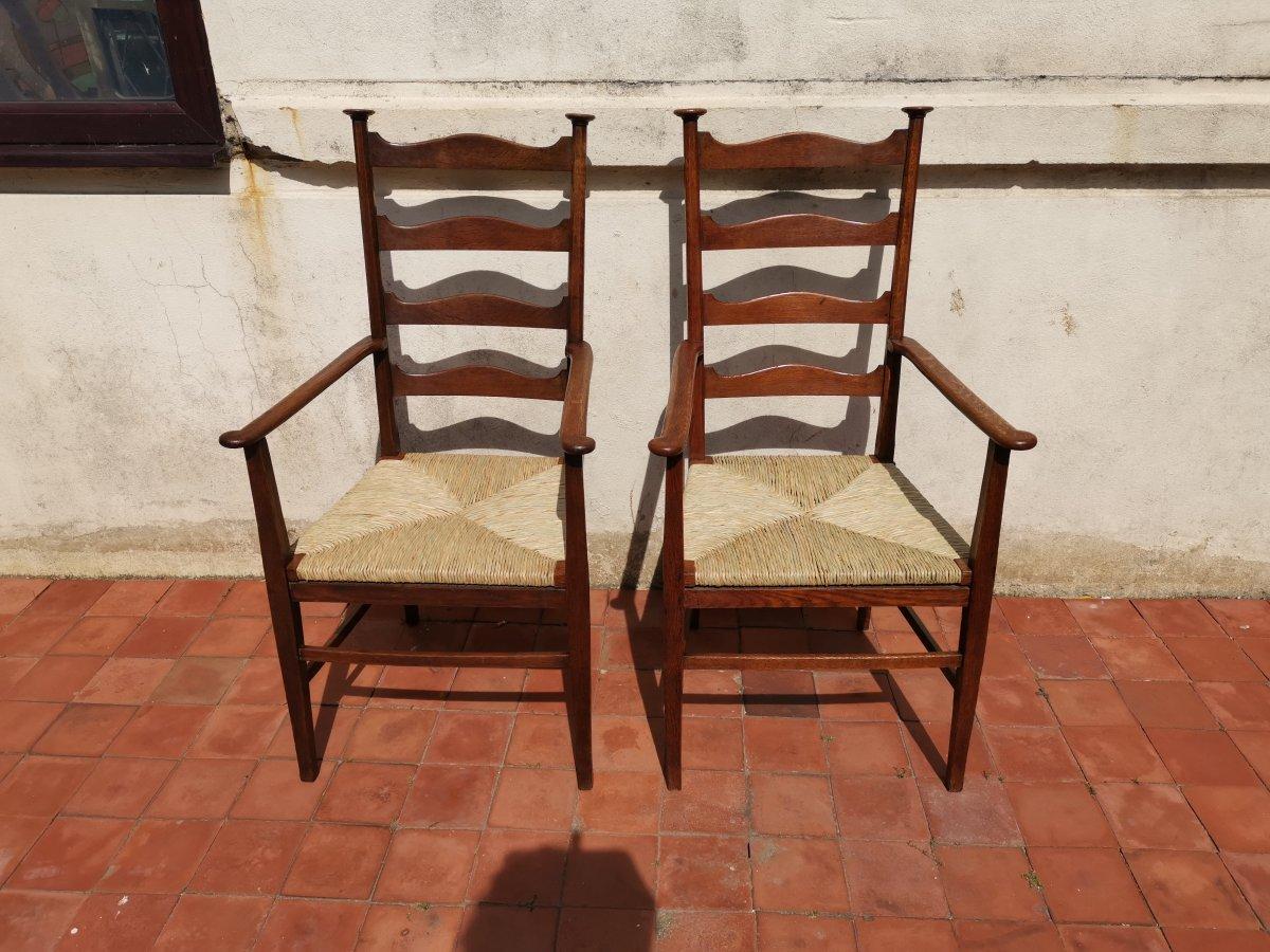 Liberty & Co, in the style of C F A Voysey.
A pair of oak rush seat ladderback armchairs with circular caps to the tops and wavy ladders to the back, the arms with subtle outward shapes to the fronts on tapering square legs.
Fully restored with