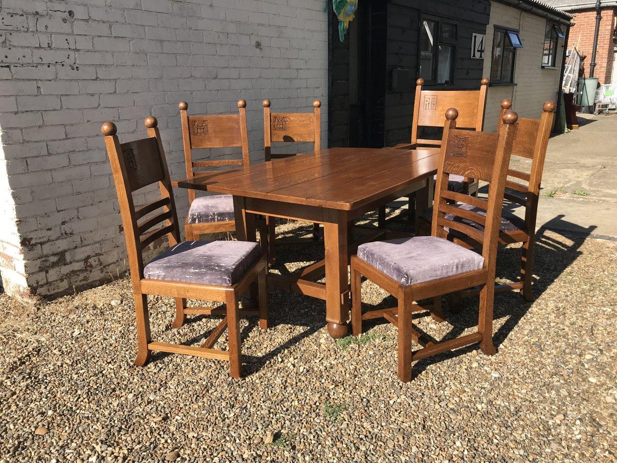 Liberty & Co in the style of CFA Voysey.
An Arts & Crafts oak dining set consisting of six chairs and a matching dining table.
The five single dining chairs have ball finials with humorous carved caricature faces to the back rests. The one