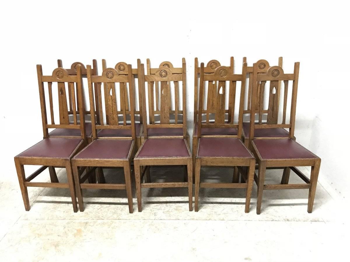 Liberty & Co, a set of ten Arts & Crafts oak high back dining chairs with floral carved roundel to the tops and stylised fret work details to the back with leather studded upholstery seats.