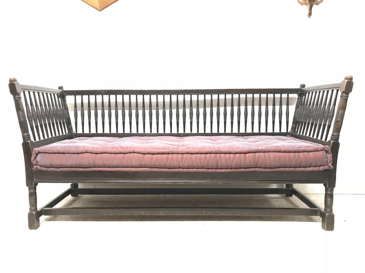 Liberty & Co, made by William Birch. An Arts & Crafts dark oak settee or sofa with turned finials, angular sides and turned uprights to the sides and to the back supports, square and turned legs united with twin stretchers below.