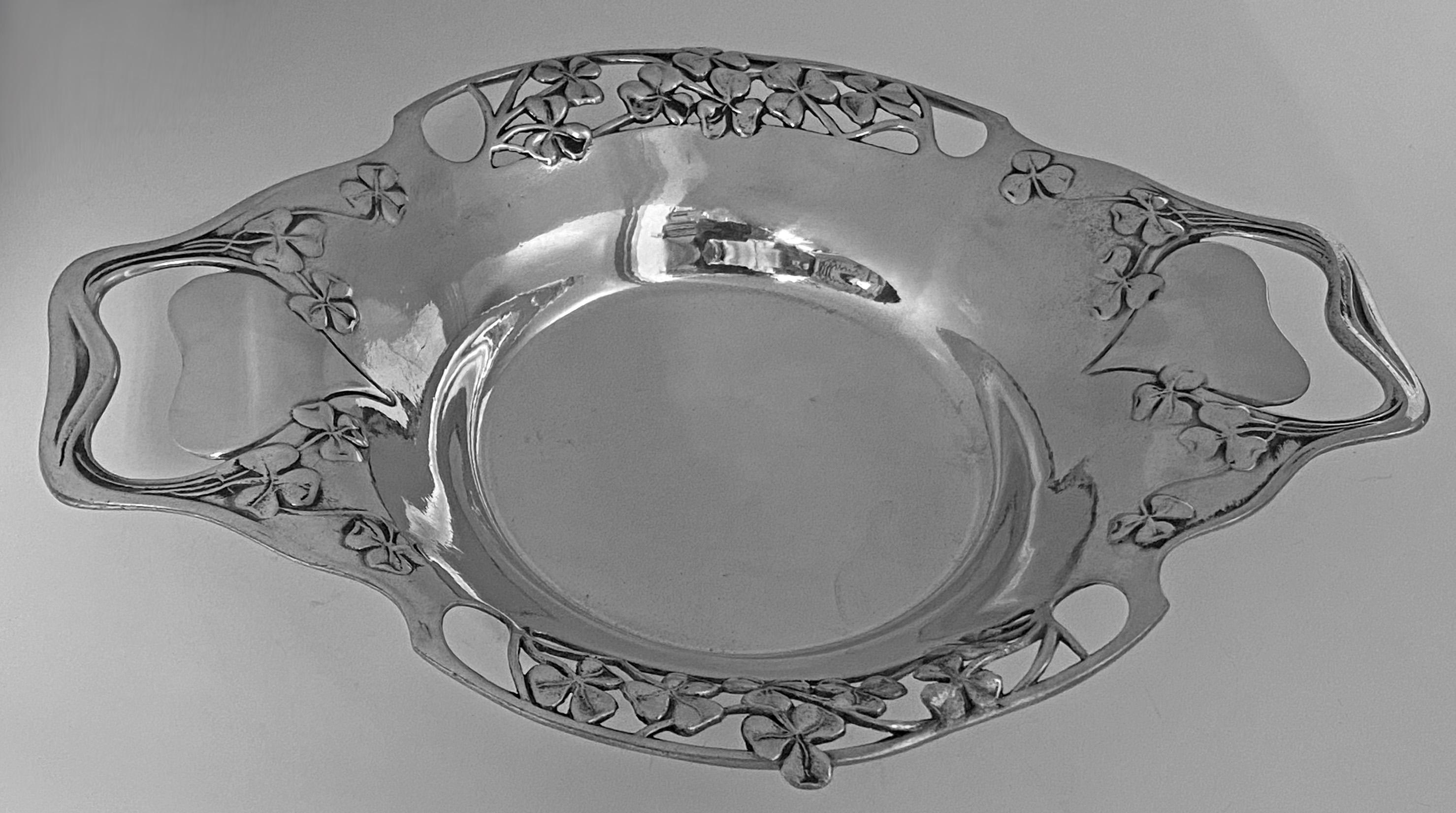 A Liberty Tudric Pewter Dish, Liberty & Co, English, circa 1903. The two handled dish with stylized cut out handles in a heart shape with a pierced surround of shamrocks, welled interior. Stamped Made in England 0287 Solkets mark on underside.