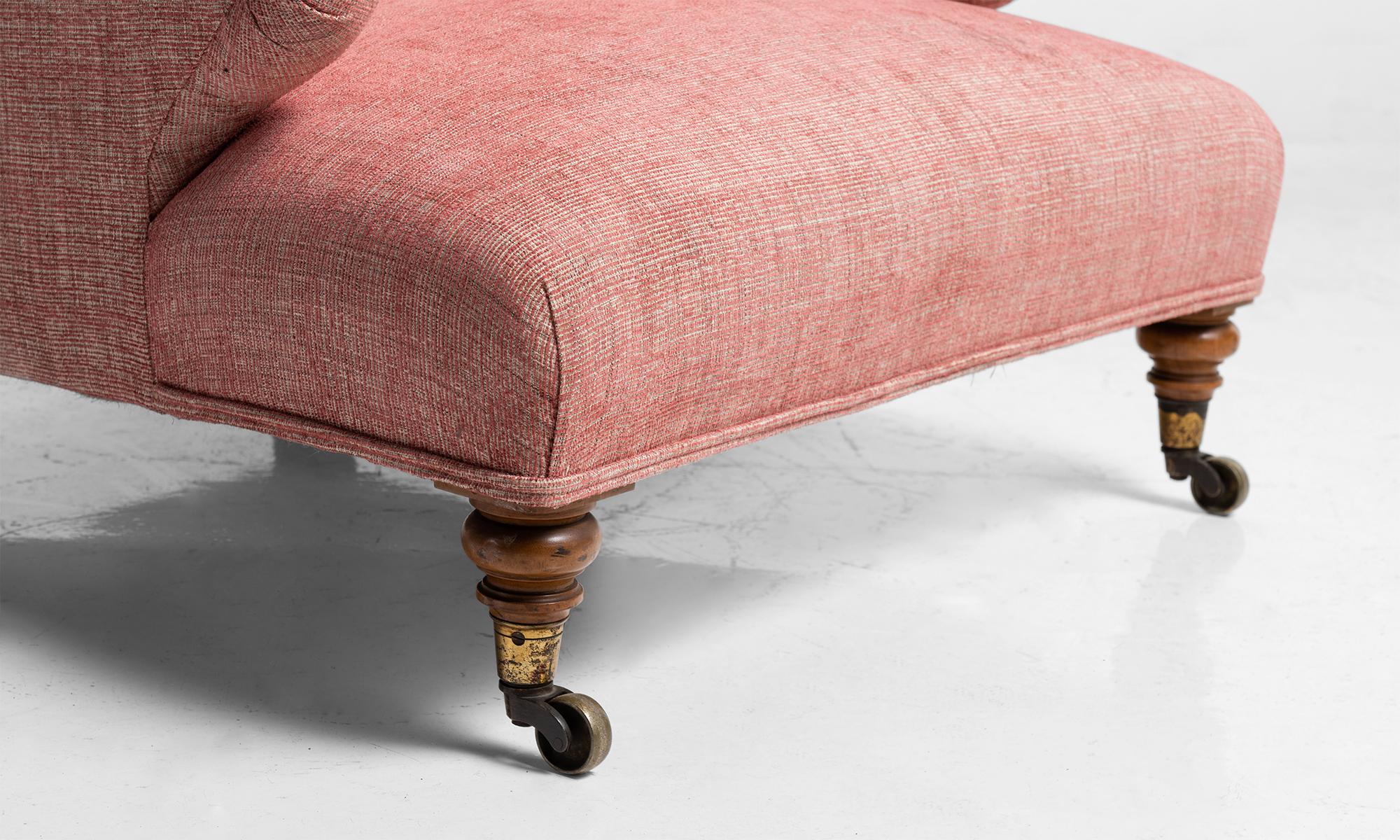Low and deep, upholstered in pink linen, with turned birch legs at the front and straight splayed back legs on original brass castors.
 