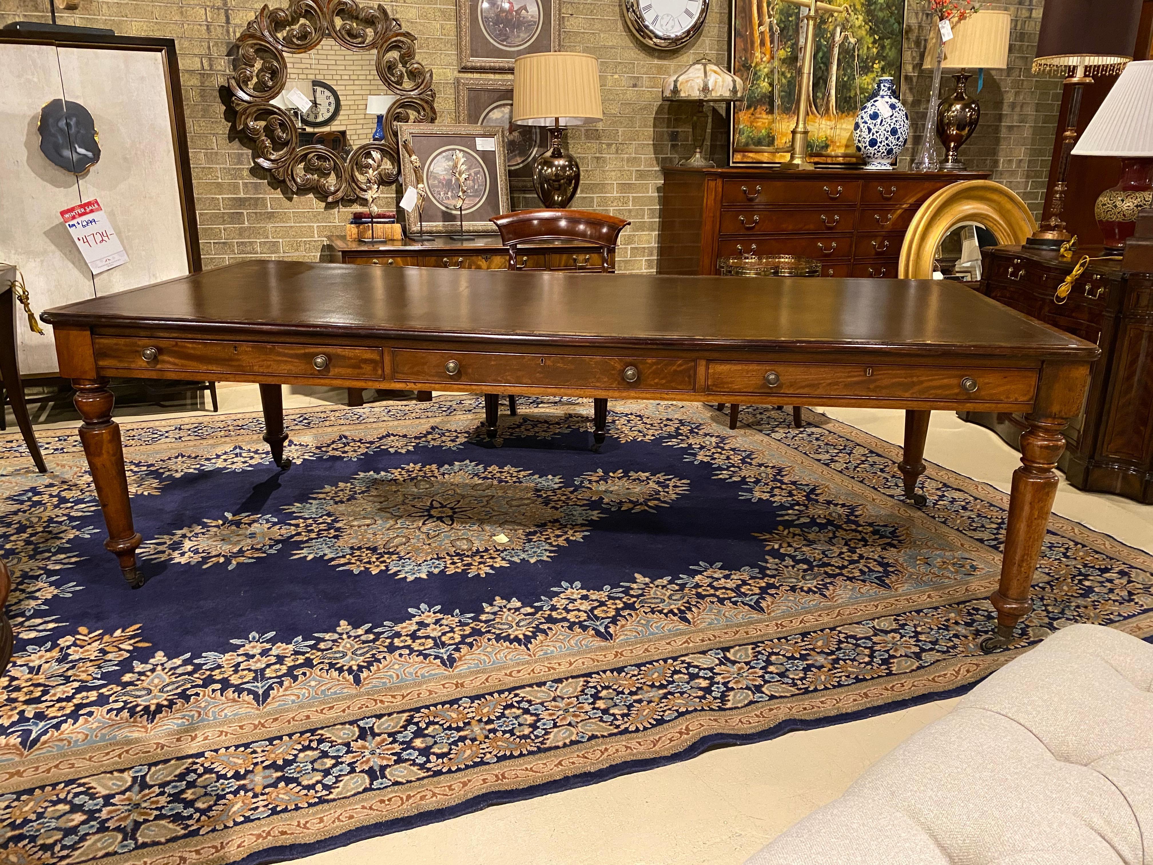 A large scale mahogany English Library table with embossed brown leather top and subtle gold tooling. Four turned legs with brass casters, there are three drawers and brass hardware on each side. The mahogany solids and veneers and the hand cut