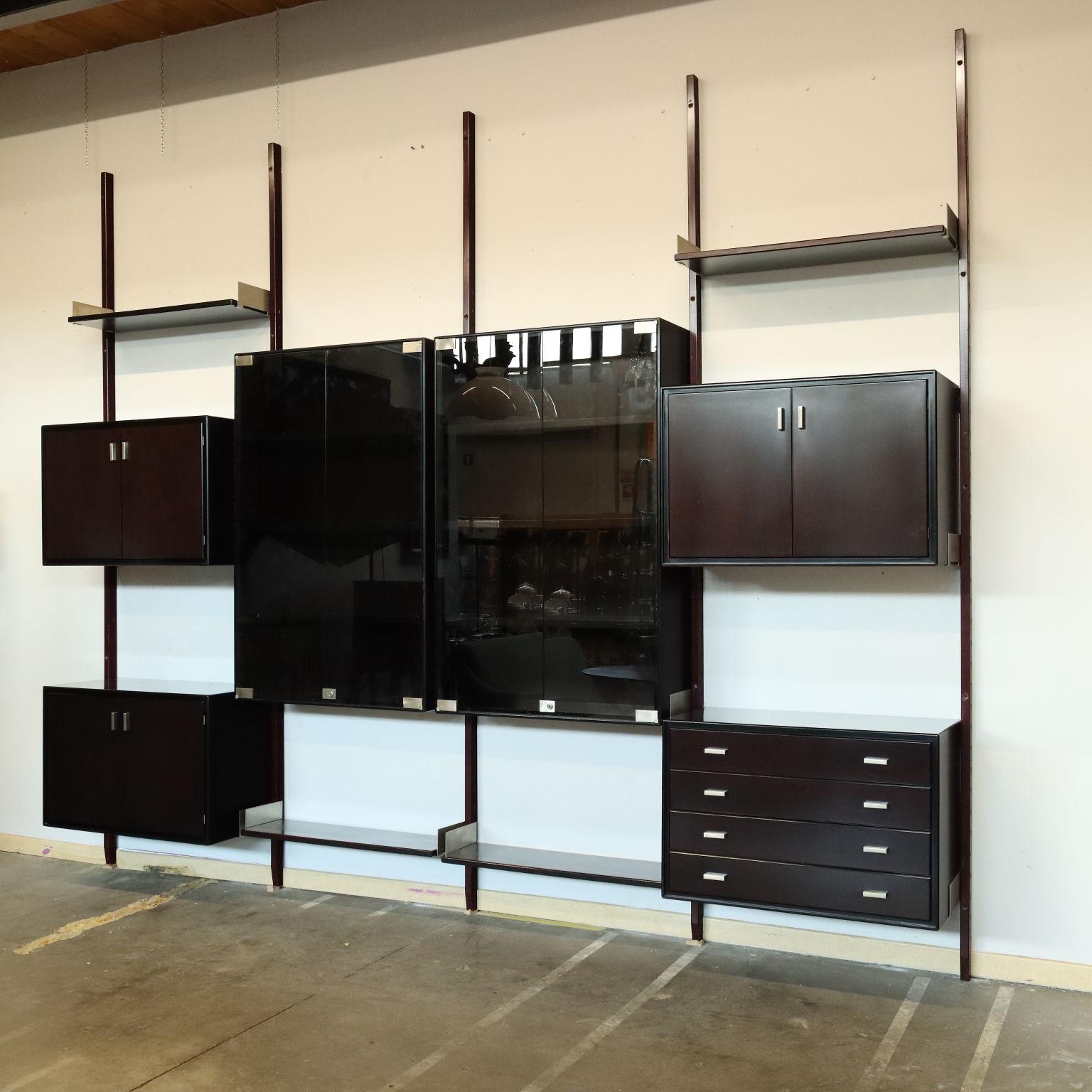 Large four-bay wall-mounted vintage bookcase with shelves, storage compartments, drawers and center display cases with adjustable position. Made of exotic wood and stained wood with metal handles and shelf attachments