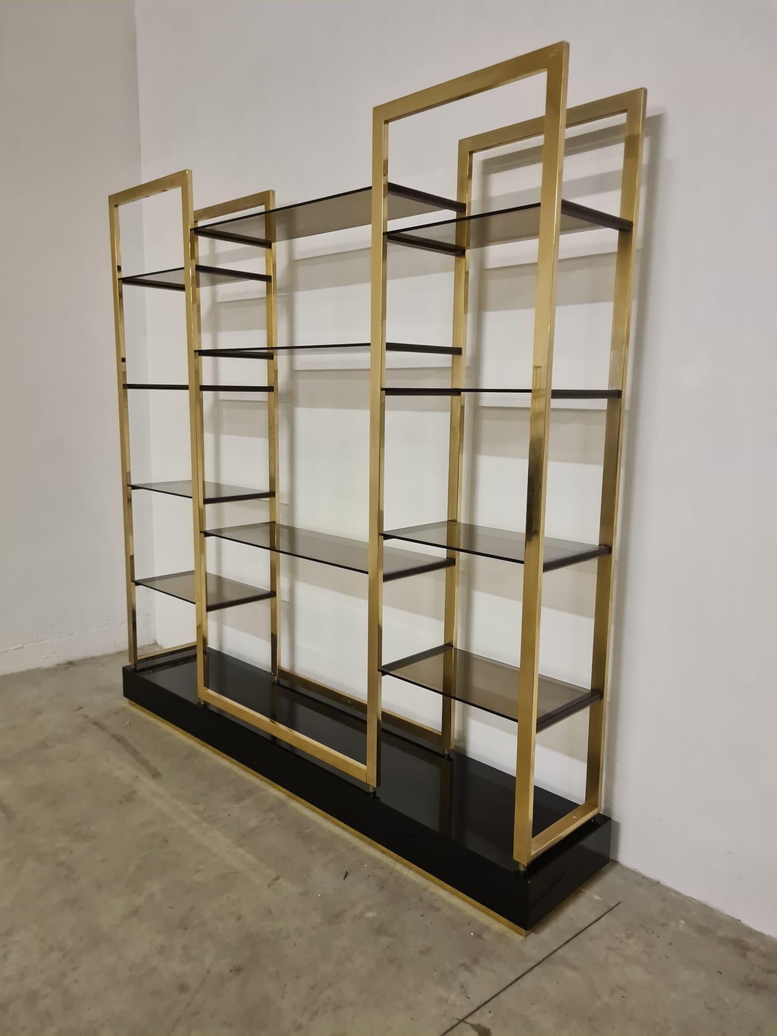 Bibliothèque autoportante conçue par Alain Delon

Élégante étagère sur pied avec base rectangulaire en bois laqué noir et détails en laiton.

Equipé de 11 étagères en verre fumé réparties en 3 colonnes, celle du centre étant la plus large.

Conçu
