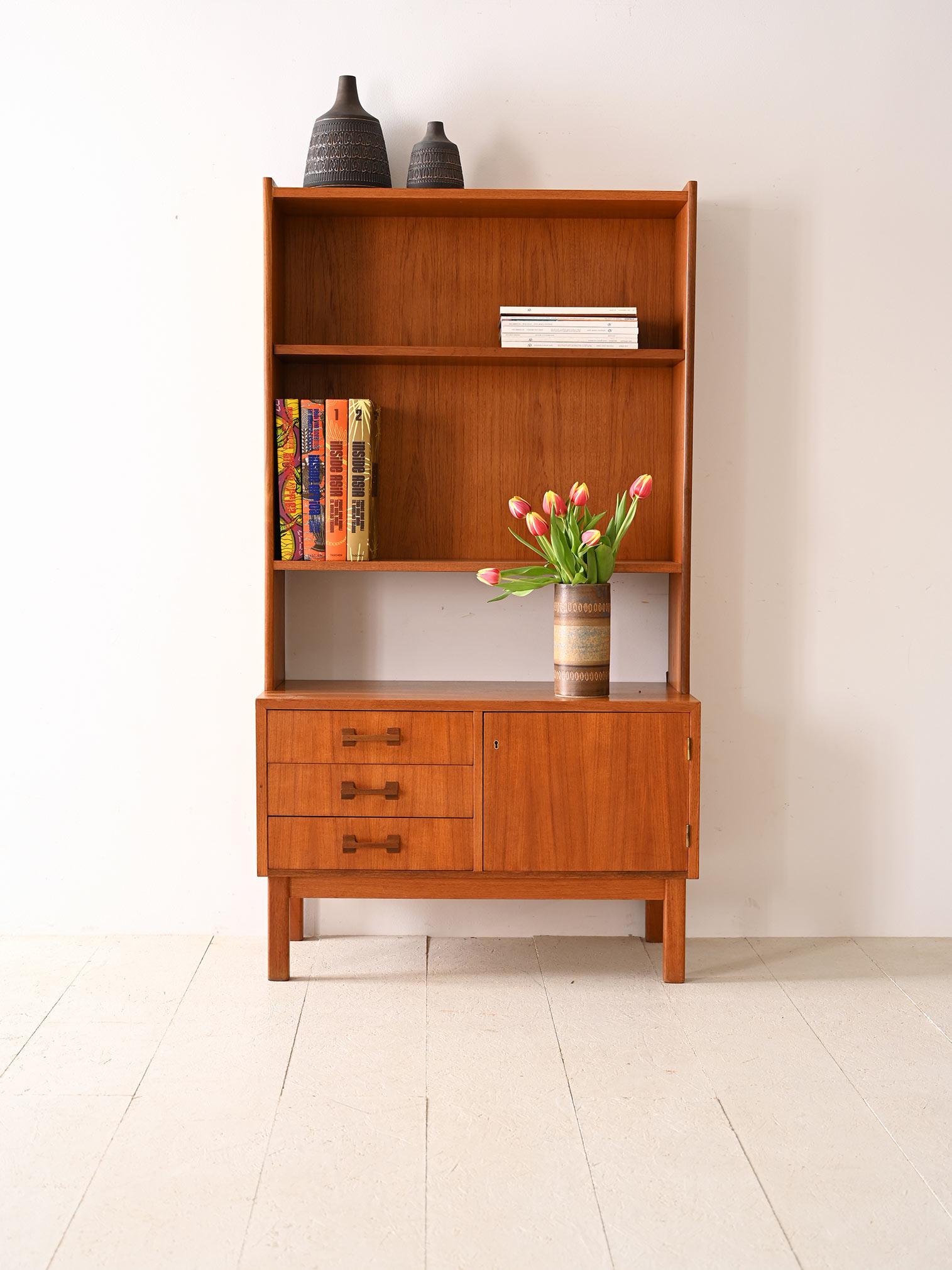 Original 1960s vintage teak cabinet with shelving. This versatile bookcase consists of a low cabinet and a shelf structure. The low cabinet features a storage space closed by a hinged door equipped with a lock and three drawers with wooden handles.