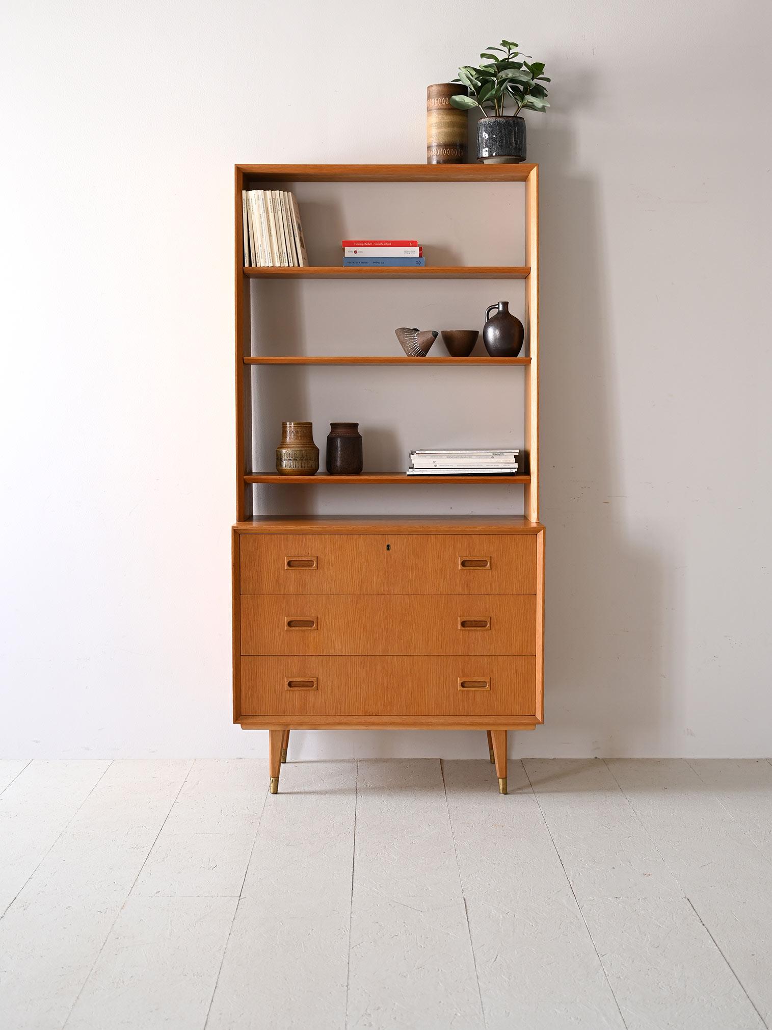 La bibliothèque en chêne nordique des années 1960 allie la simplicité du design à la fonctionnalité quotidienne.
Le meuble comporte trois tiroirs avec des poignées en bois sculpté.
Les étagères supérieures ouvertes et aérées offrent un large espace