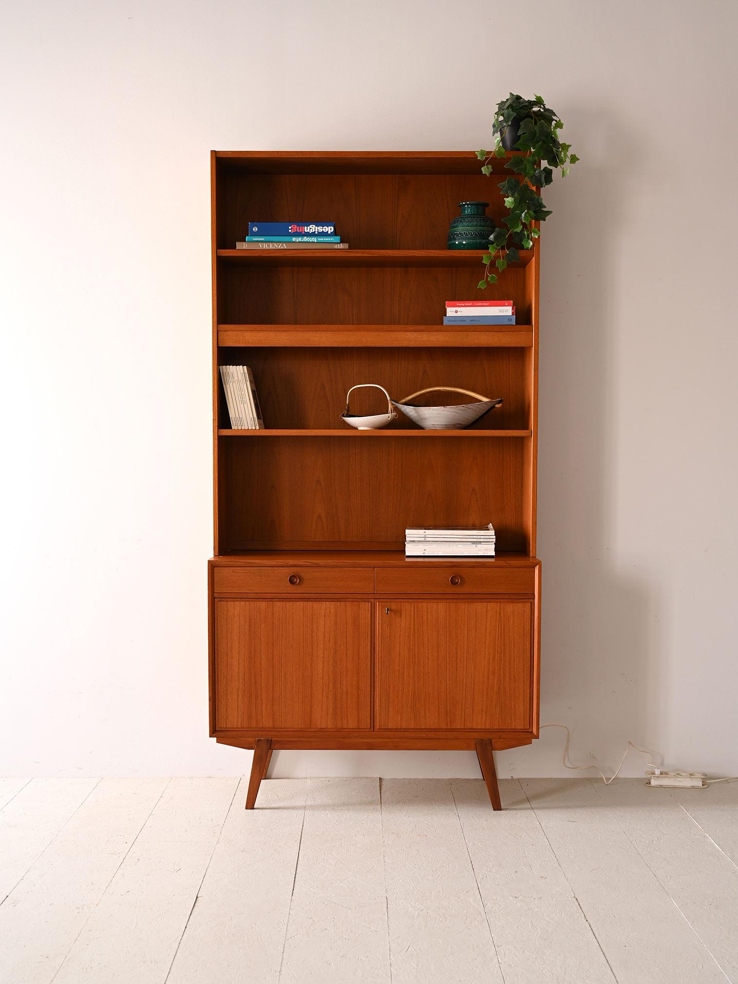 This Scandinavian teak wood bookcase, dating from the mid-century design period, offers a combination of aesthetics and functionality. At the top, three spacious shelves are illuminated by a central light point, creating an ideal display for