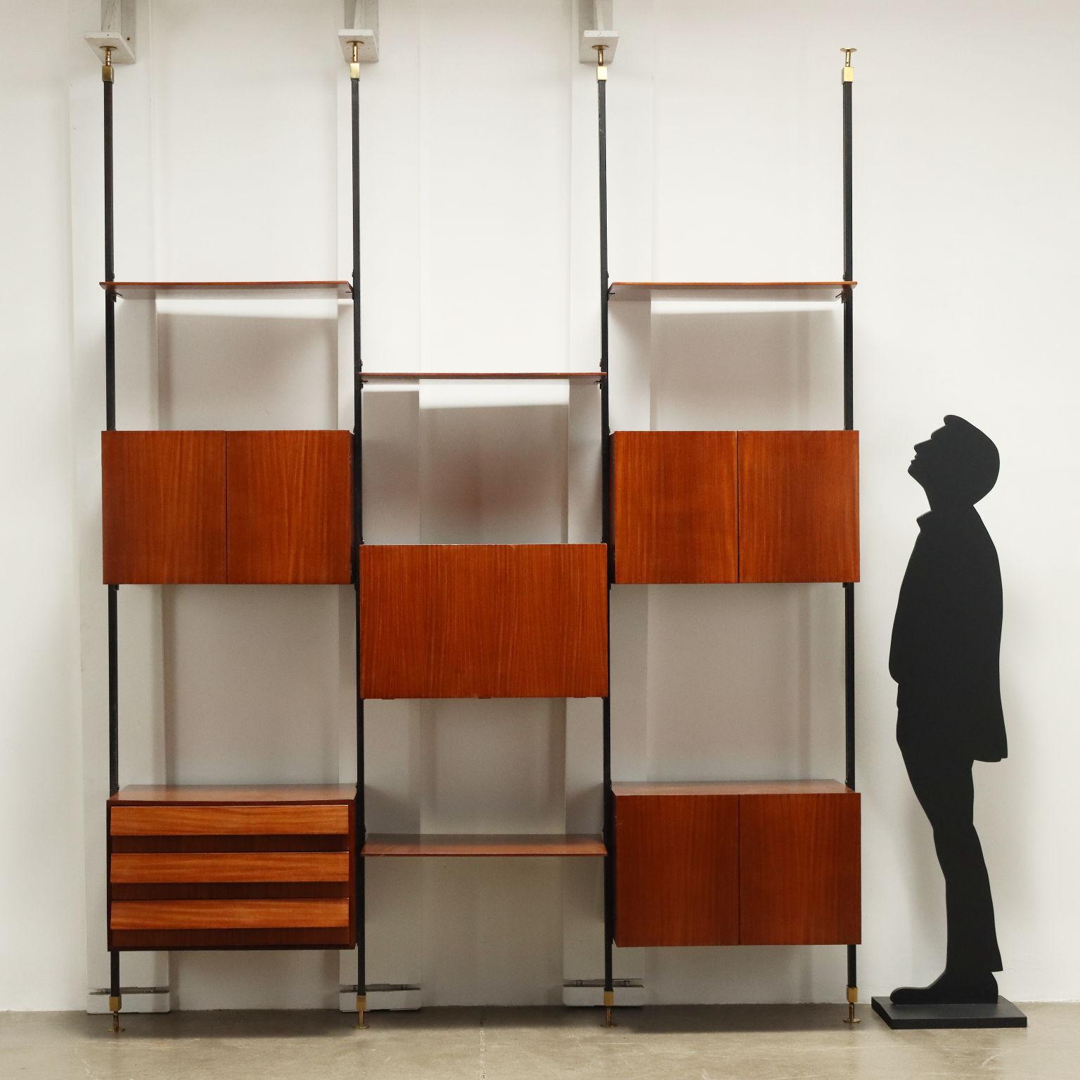 Libreria da centro a soffitto, con elementi contenitore e ripiani a posizione regolabile, aperture a battenti, ribalta e cassetti a vista, legno impiallacciato teak, montanti in metallo smaltato con terminali in ottone. Completamente restaurata. 