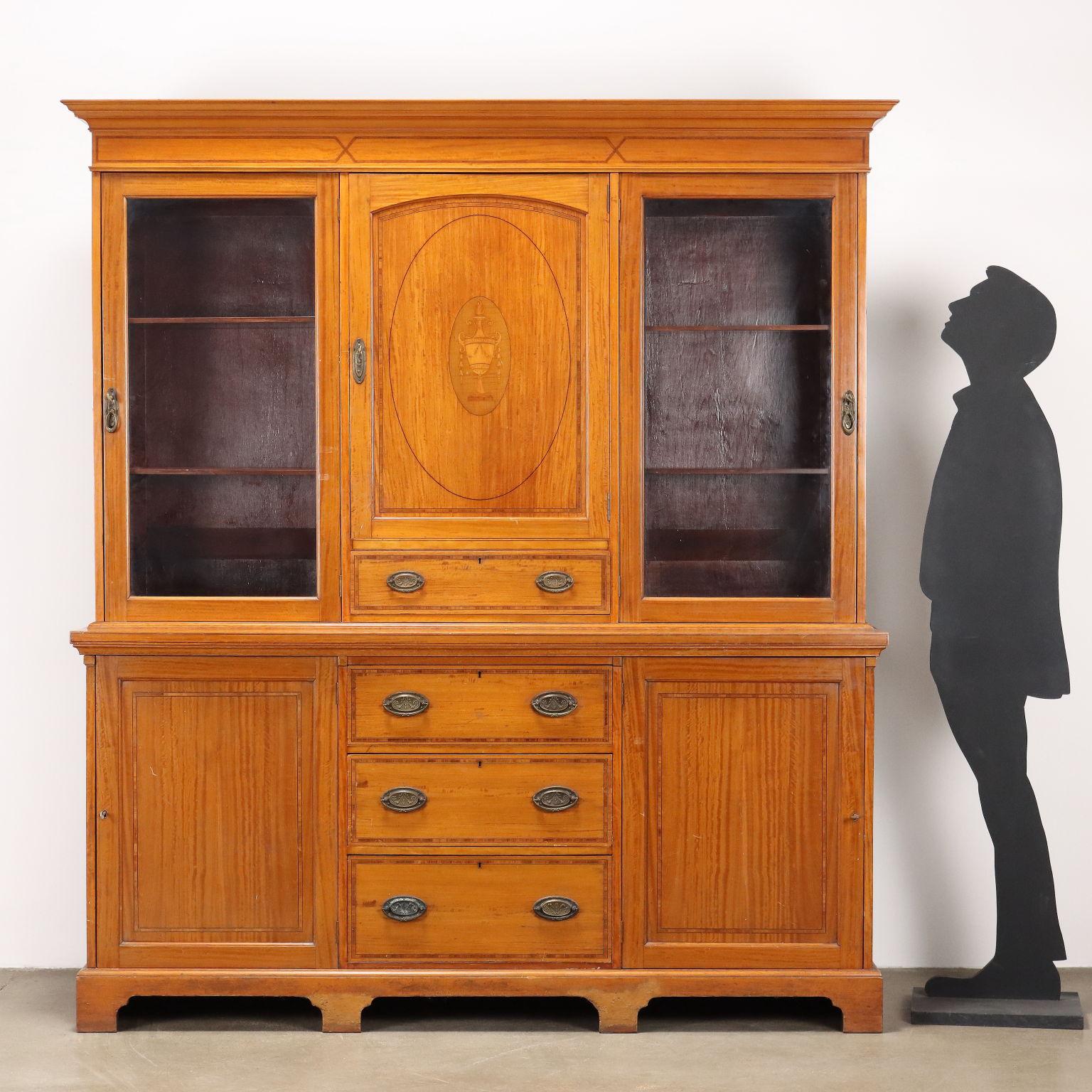 Libreria in stile Neoclassico in citronnier, base con ante pannellate laterali e tre cassetti centrali, alzata con ante a vetro laterali, centralmente presenta un cassetto e anta pannellata intarsiata con vaso. Filettature in ebano e bois de rose in