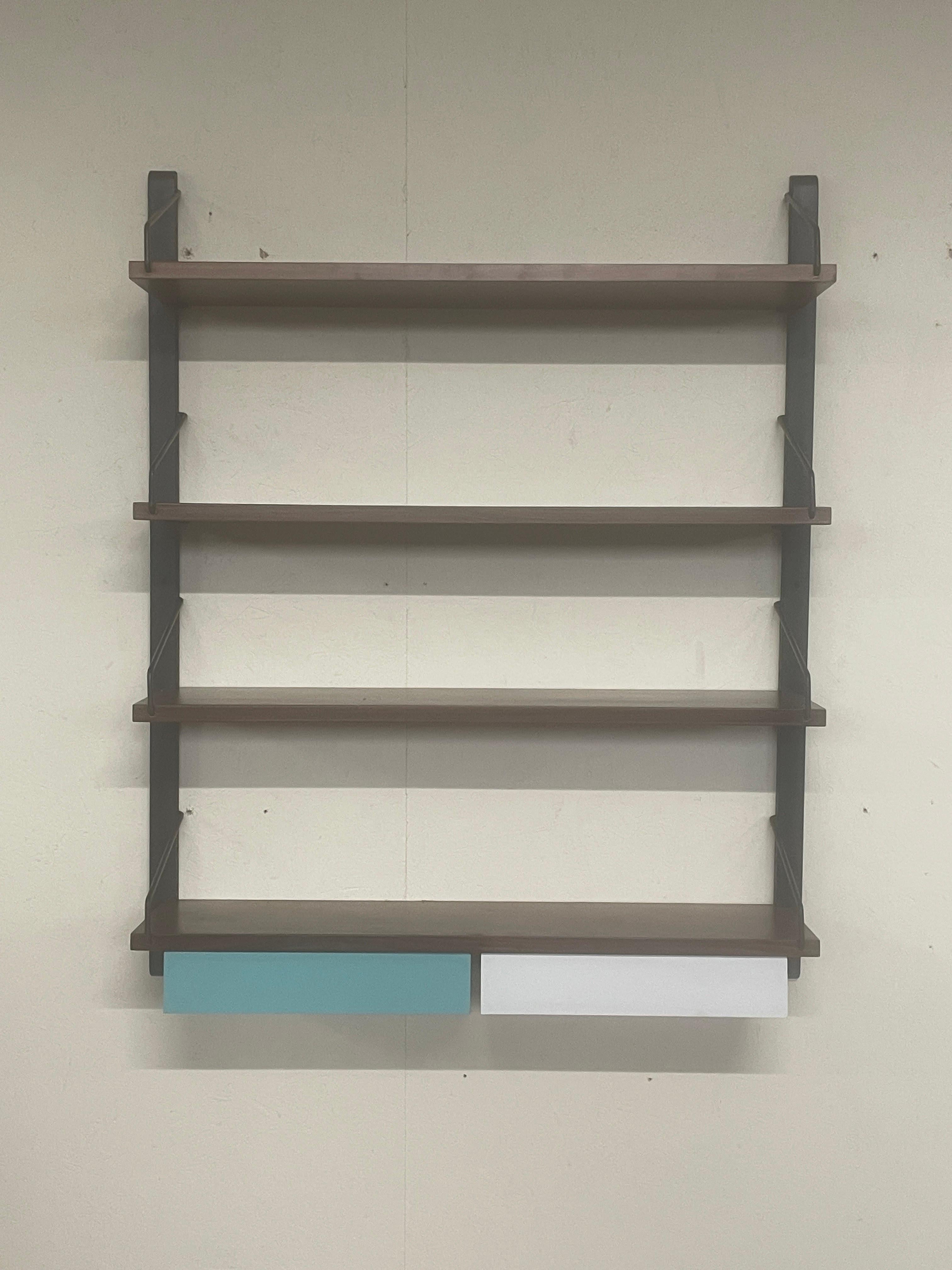 Pequeña librería colgante de los años 60 con cuatro estantes de madera de teca y dos cajones pequeños con frentes de formica de colores.

Montantes laterales de hierro.

Una librería ágil que puede convertirse en una cómoda solución para todas las