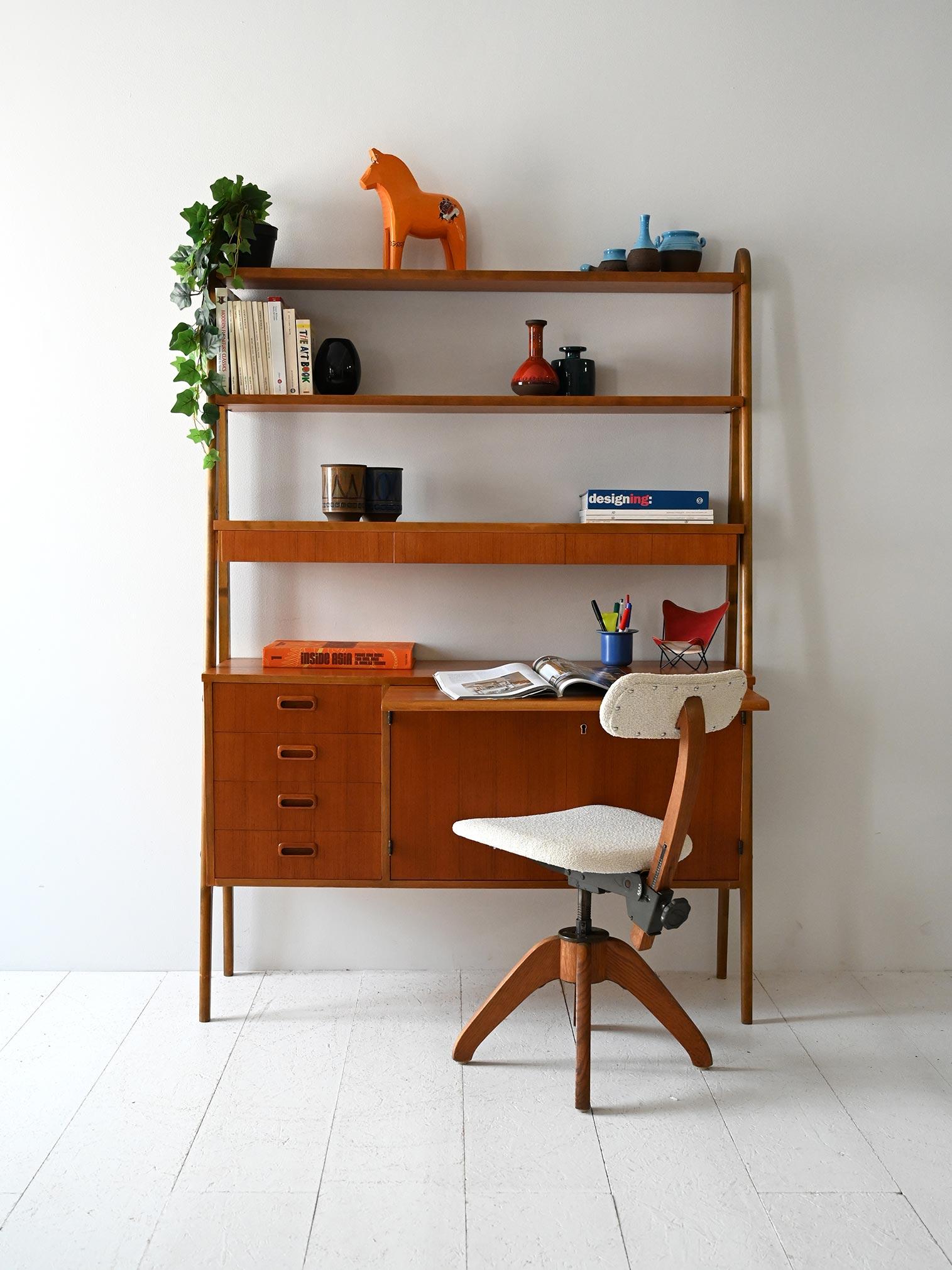 Vintage bookcase with teak frame, hideaway desk and hanging storage modules.

Scandinavian 1950s/60s teak bookcase with lightweight upright frame. The lower part integrates a drop-down desk and a sideboard module, while the upper part contains open