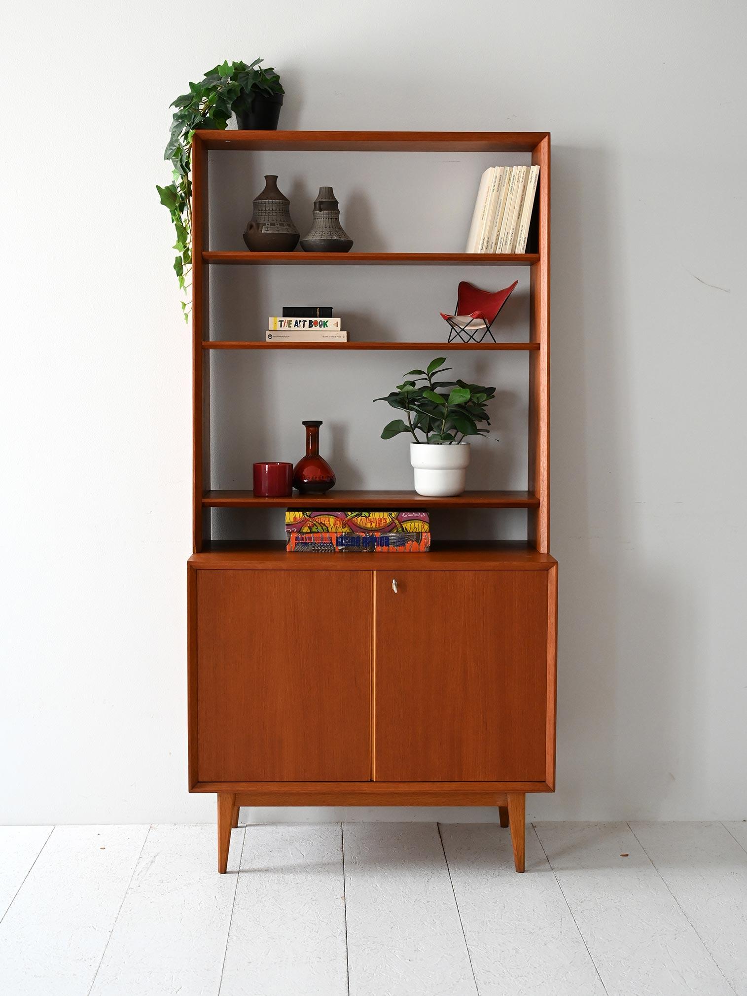Vintage bookcase with teak frame, short oblique legs, closed compartment with doors and upper part with open shelves.

Original Scandinavian teak bookcase from the 1960s, characterized by short, oblique legs, slender frame and well-balanced