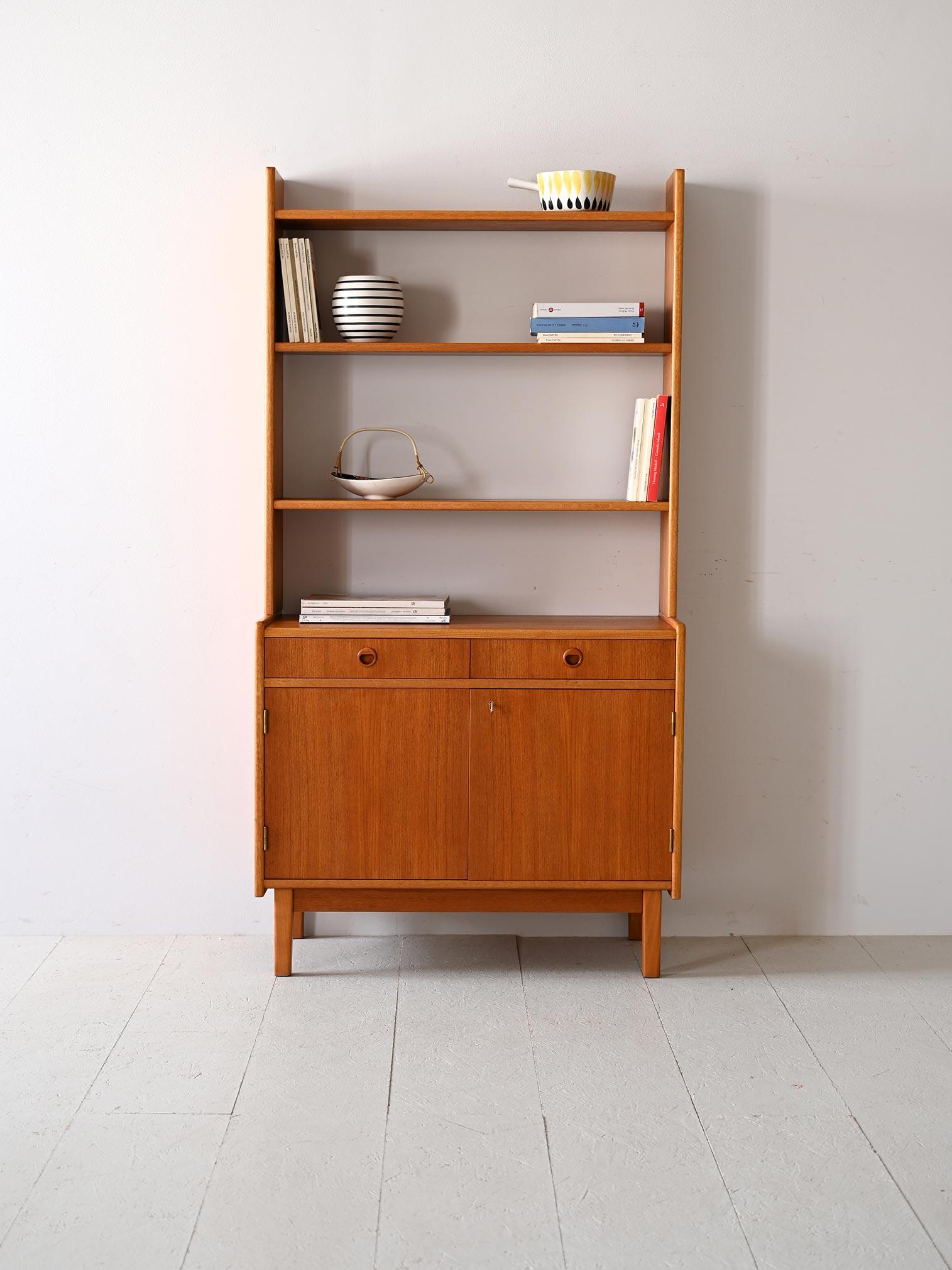 A vintage Scandinavian teak bookcase, characterized by clean lines and an essential silhouette that testifies to the functional aesthetic typical of Nordic design of the last century. 
This bookcase features doors and drawers that offer practical