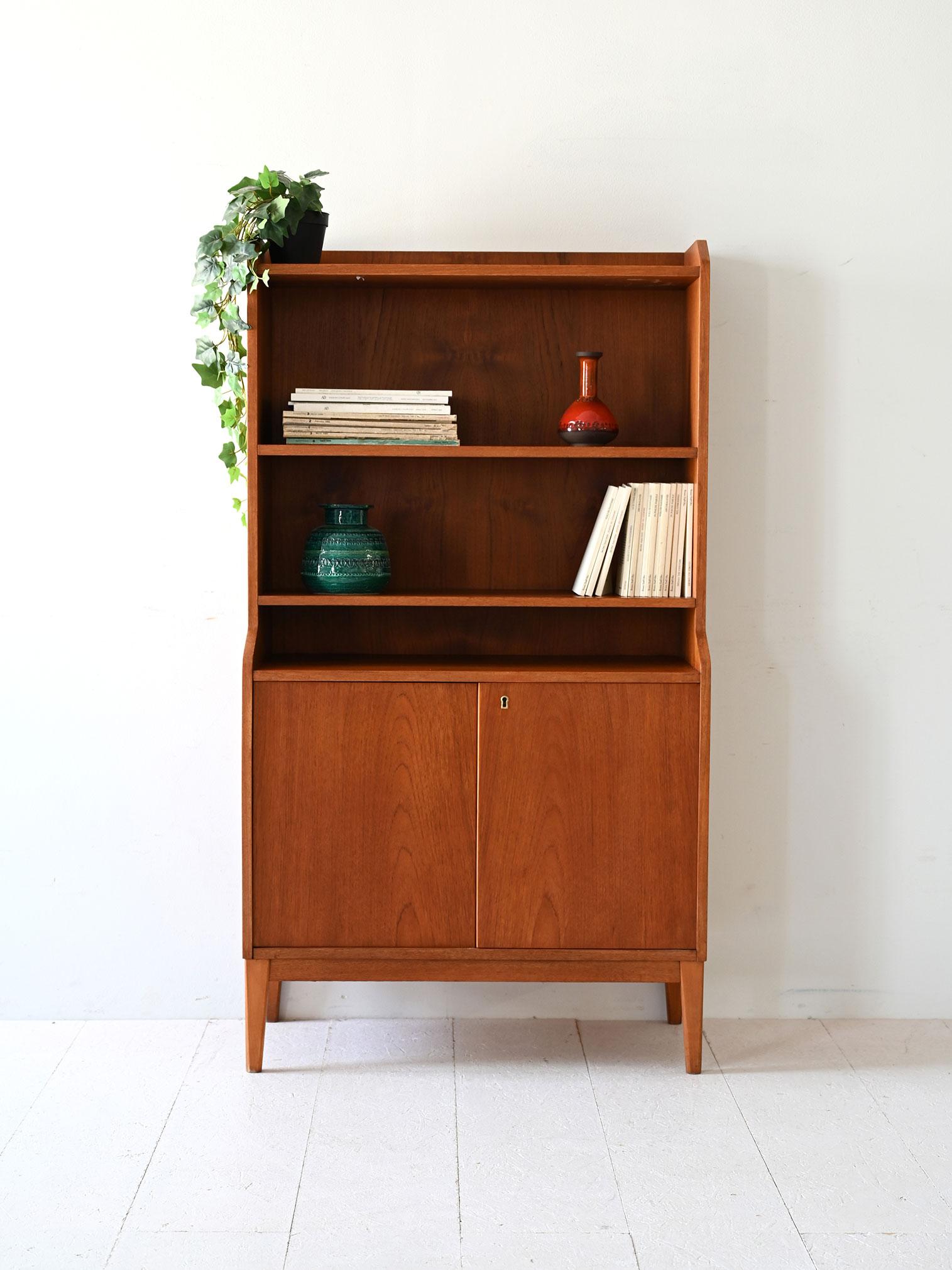 Élégante bibliothèque en teck des années 1950 avec trois étagères ouvertes et un compartiment fermé par des portes à charnières.

Bibliothèque vintage scandinave en teck, fabriquée à la fin des années 1950. La structure comporte trois étagères dans