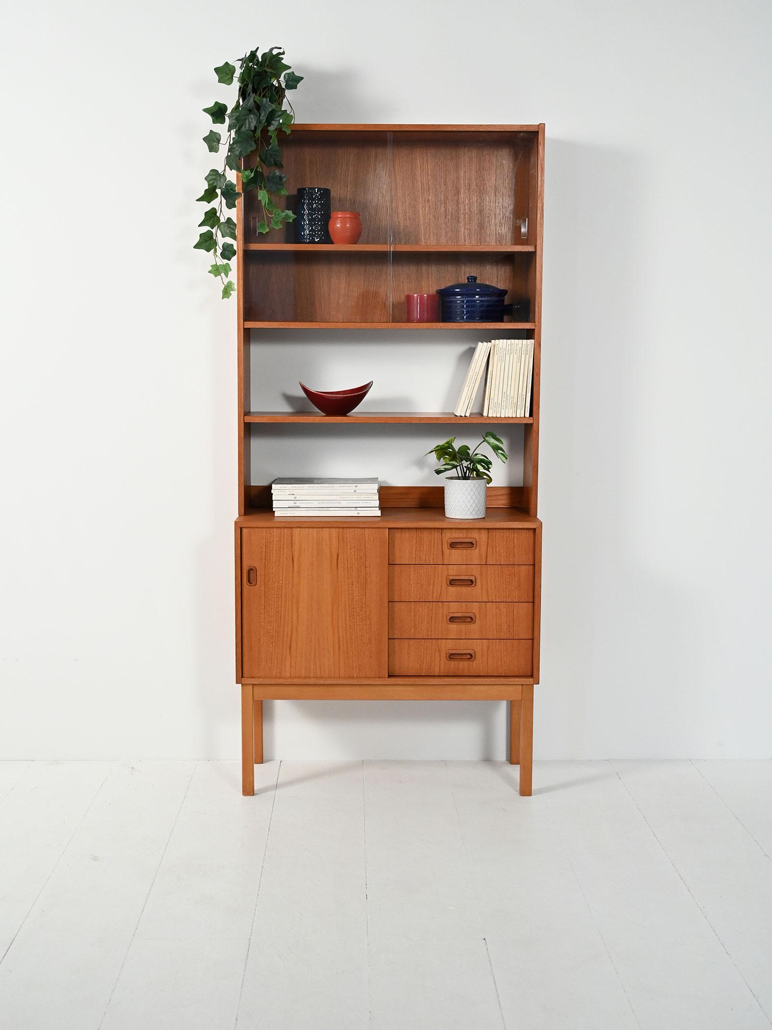 Libreria scandinava anni ’50/’60 in teak: base con anta scorrevole e quattro cassetti, parte alta con mensola a vista e vetrinetta.

Elegante libreria scandinava anni ’50/’60 in teak, dal profilo sottile e proporzioni slanciate. La base comprende un