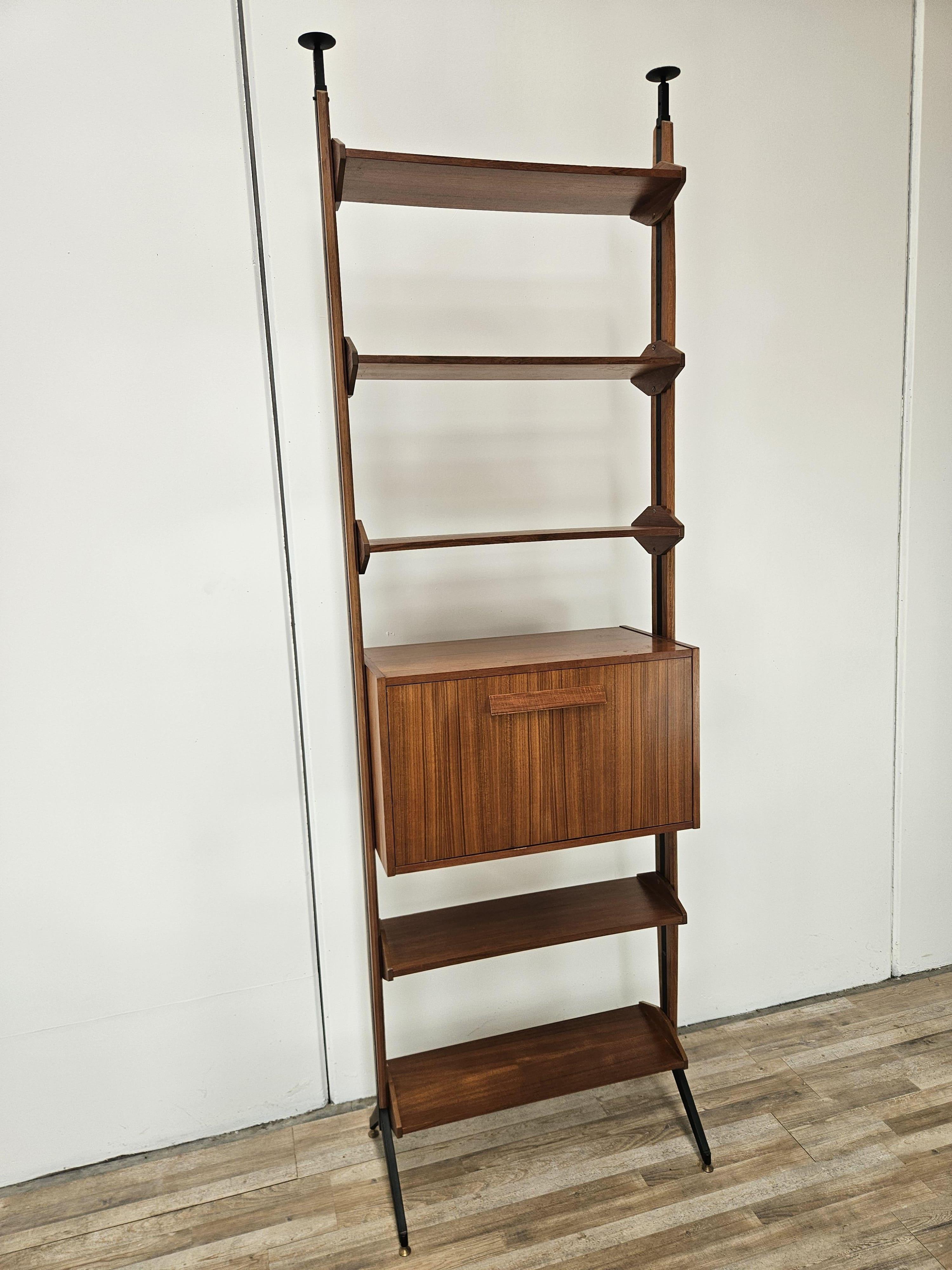 Libreria anni '60 impiallacciata in teak con struttura e montanti in ferro e piedi regolabili in ottone.

Il mobile dispone di diversi fori lungo le due strutture così da poter spostare le mensole a proprio piacimento.
Arricchito inoltre da un vano