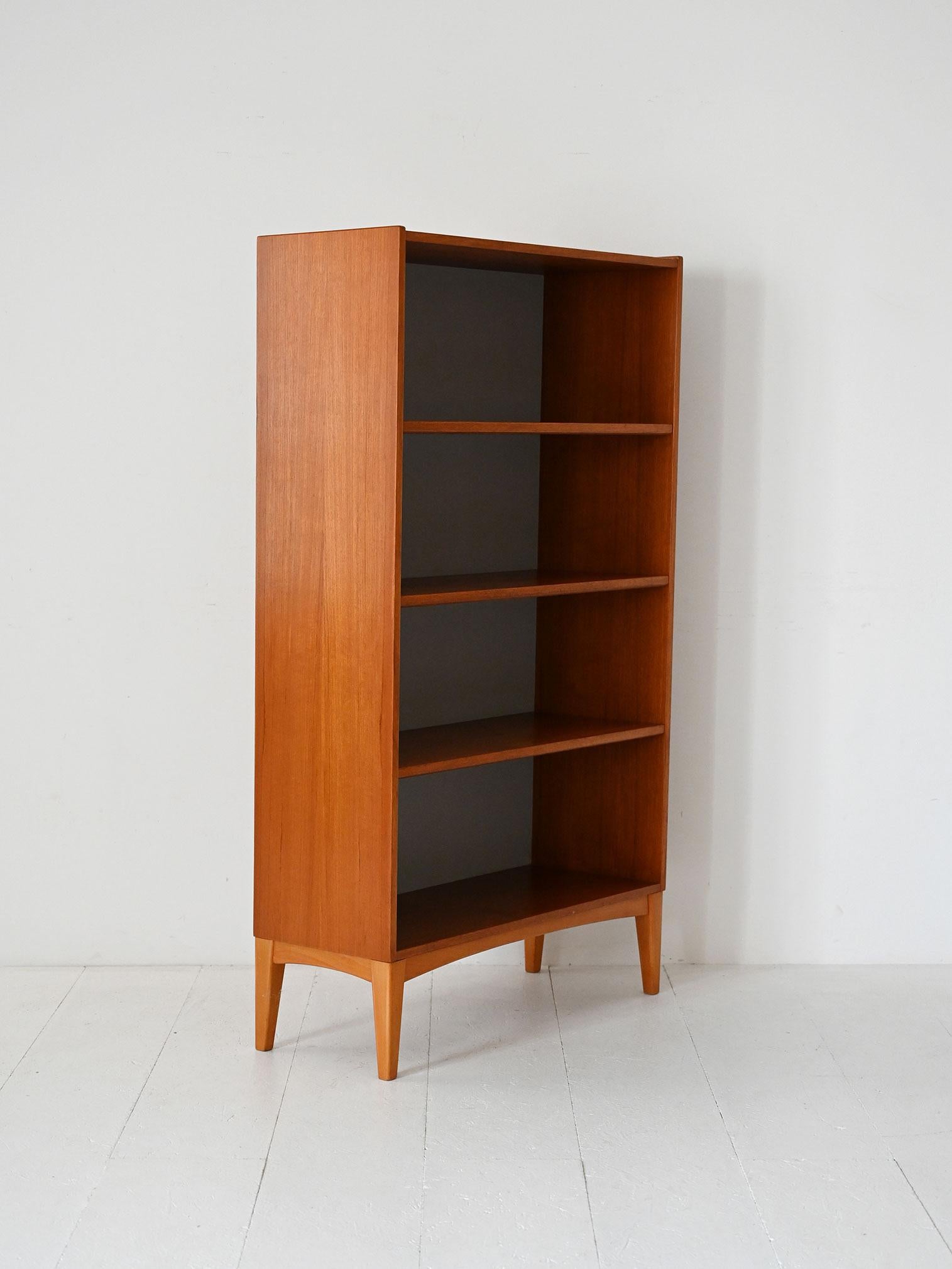 Bibliothèque en teck des années 1950 avec étagères apparentes, fond gris et pieds qui donnent de la légèreté à la structure.

Bibliothèque scandinave vintage des années 1950 en teck. La structure linéaire est caractérisée par un fond gris qui