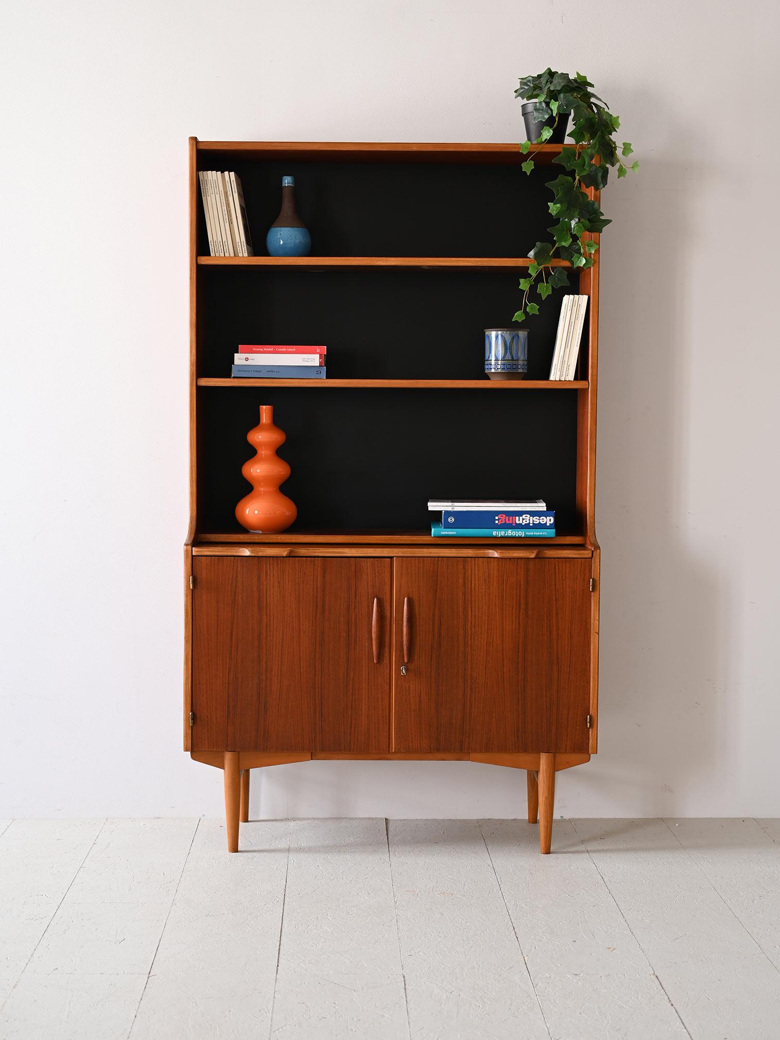 Teak cabinet with shelving and storage compartment.

This Scandinavian bookcase from the 1960s, thanks to its pull-out shelf and storage compartment closed by hinged doors, offers functionality and style in a compact space. 
The open shelves lend