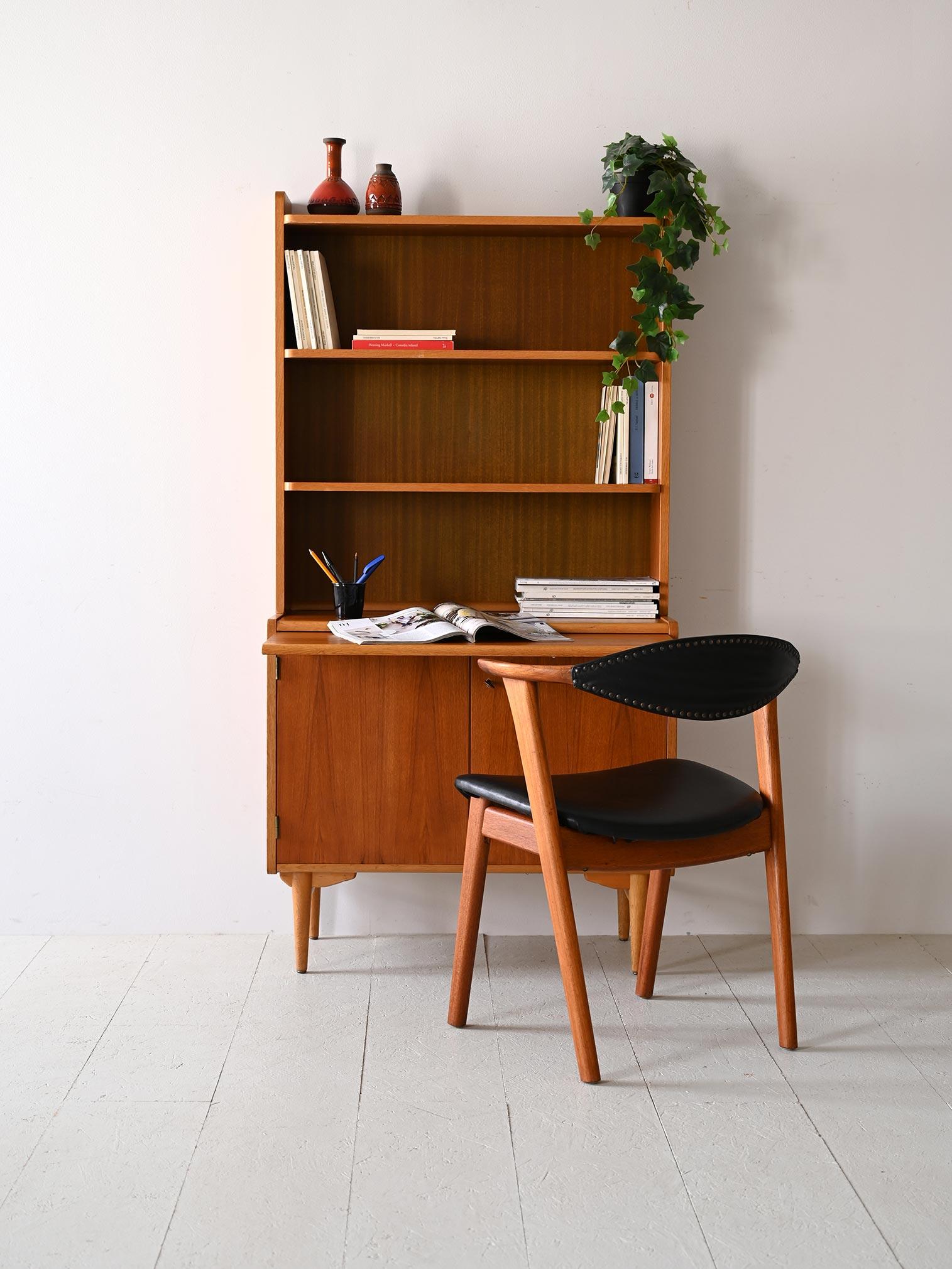 Scandinavian cabinet with shelving and storage compartment.

This Nordic teak bookcase features a frame with open shelves that rests on the cabinet with hinged doors.
There is also a pull-out shelf that provides an additional surface for support or
